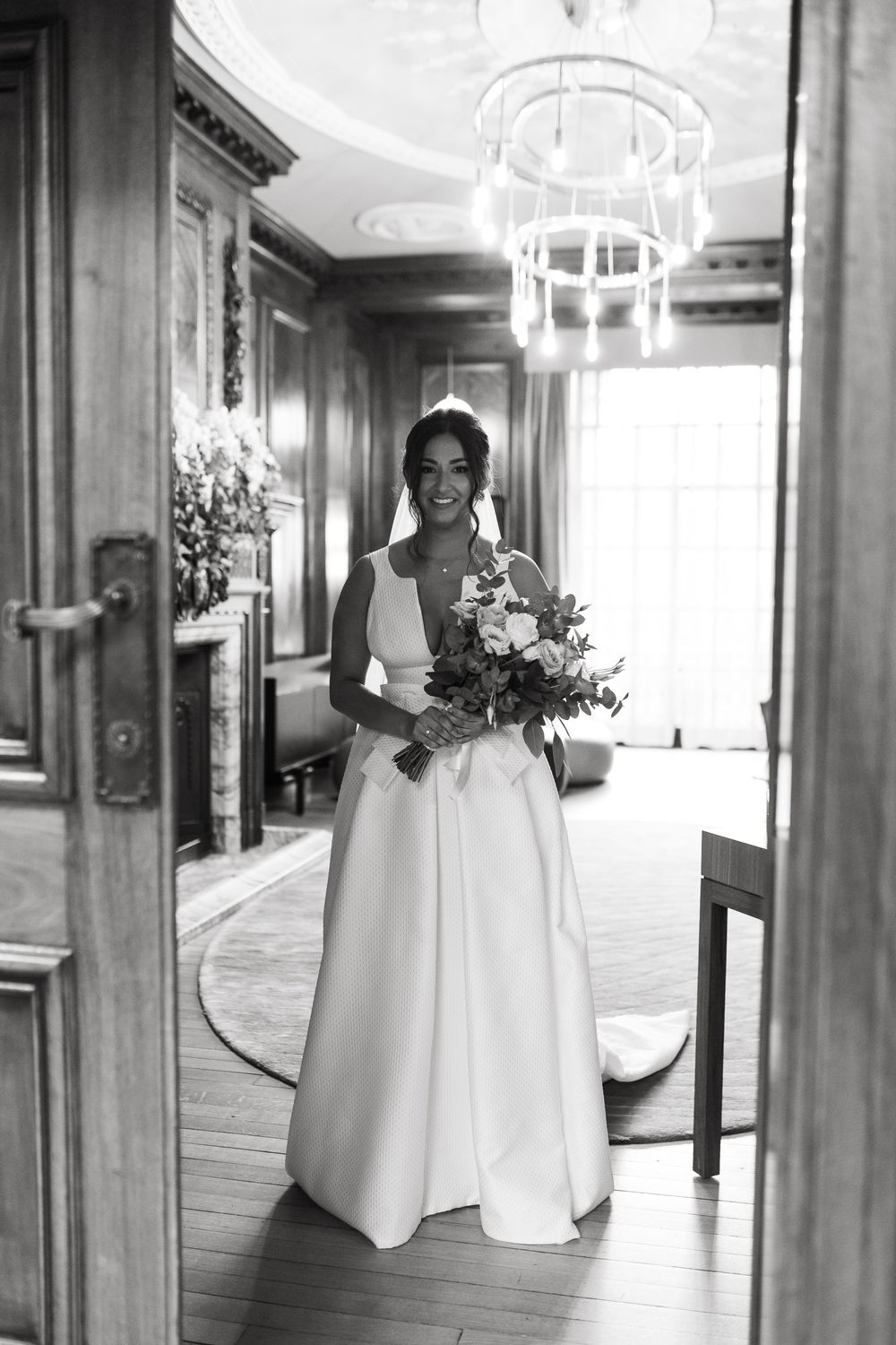 Elegant bridal party walks through a hallway with chandelier lighting.