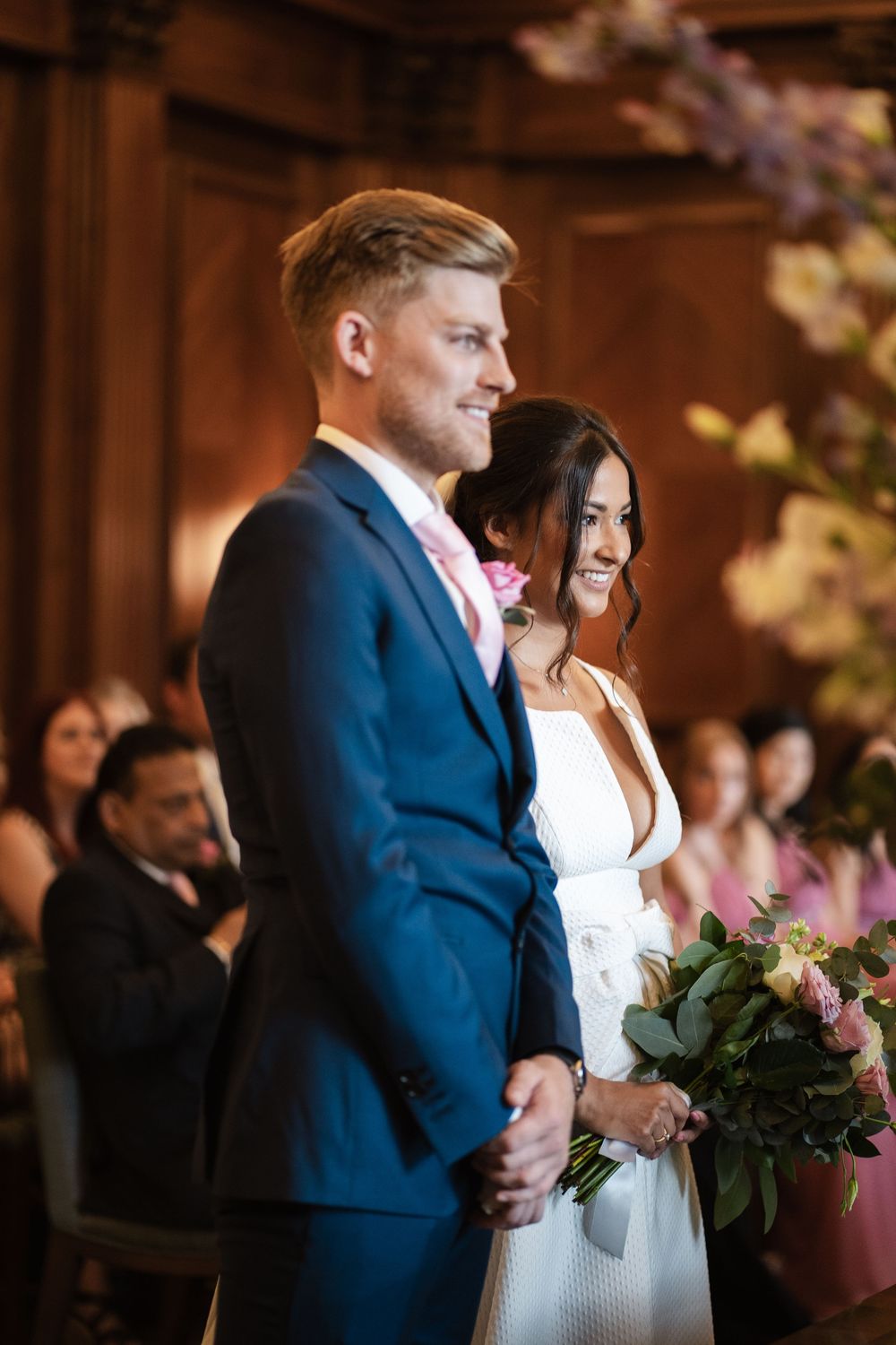 Newlyweds stand together elegantly during their wedding ceremony in a beautifully decorated wood-paneled venue.