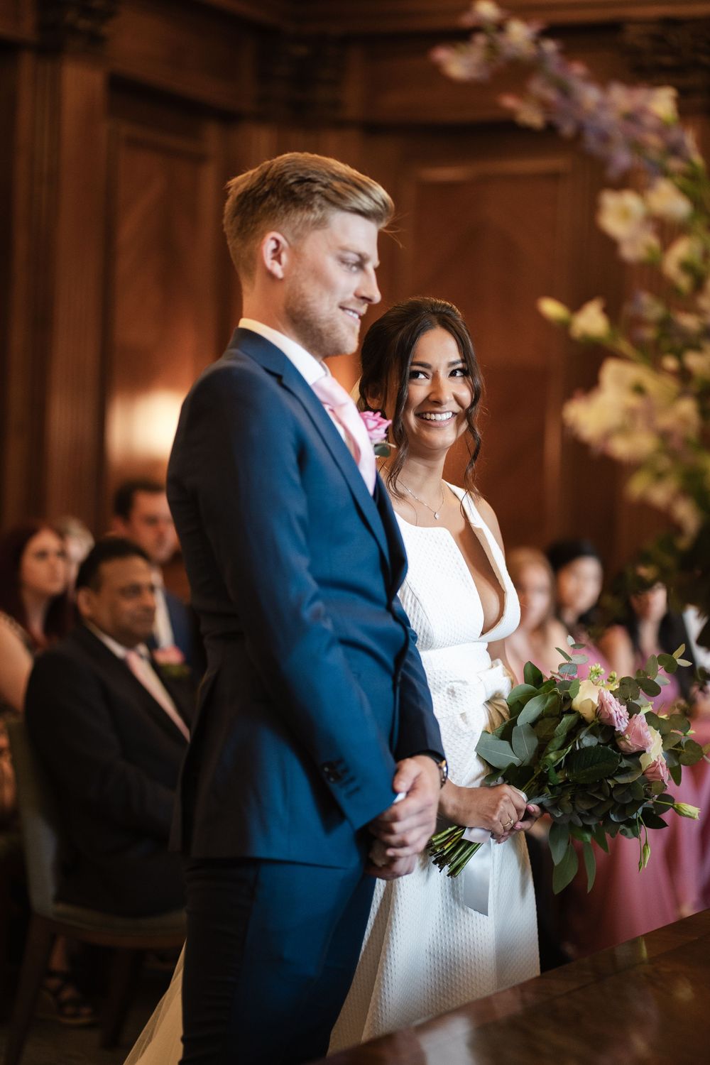 A couple shares a joyful moment during their wedding ceremony at an elegant indoor venue with floral decorations.