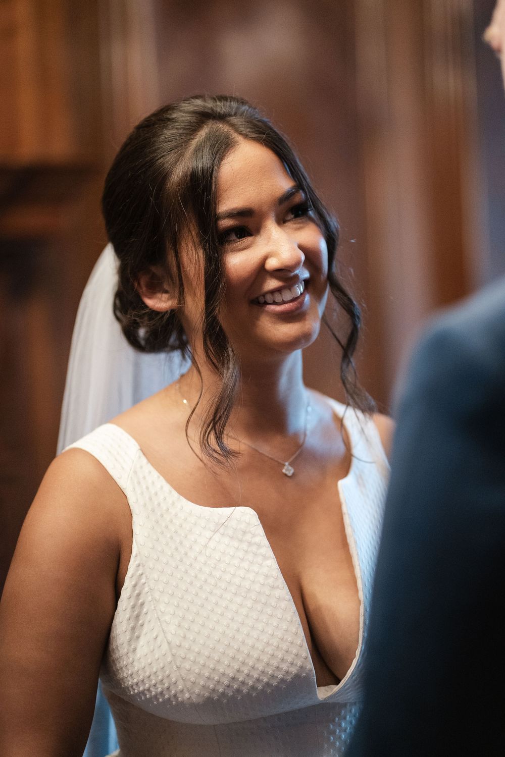 Close-up portrait of a radiant bride in a textured white wedding gown with soft makeup and loose curls.