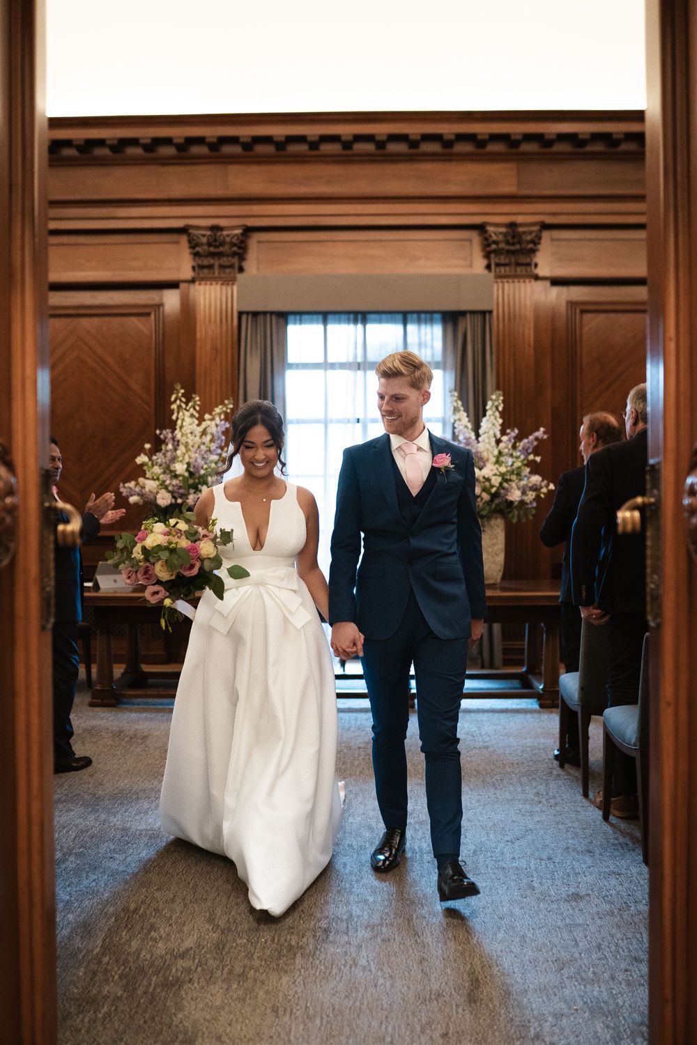 A couple walks down the aisle together in a wood-paneled ceremony space with elegant decor.