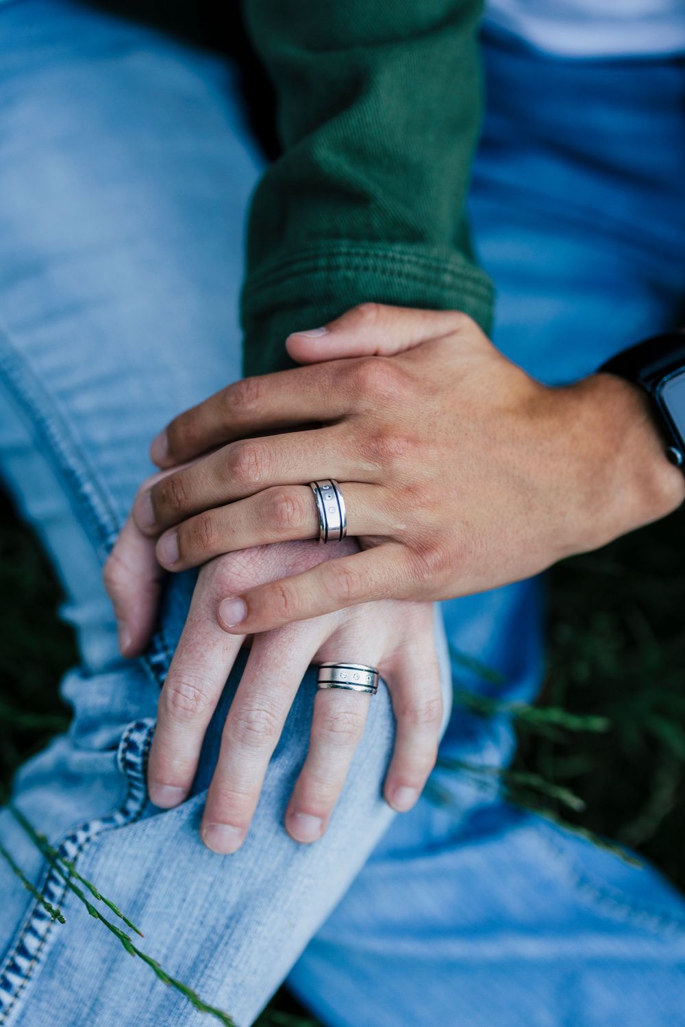 Close up shot of two hands with matching silver wedding bands resting on blue denim jeans.