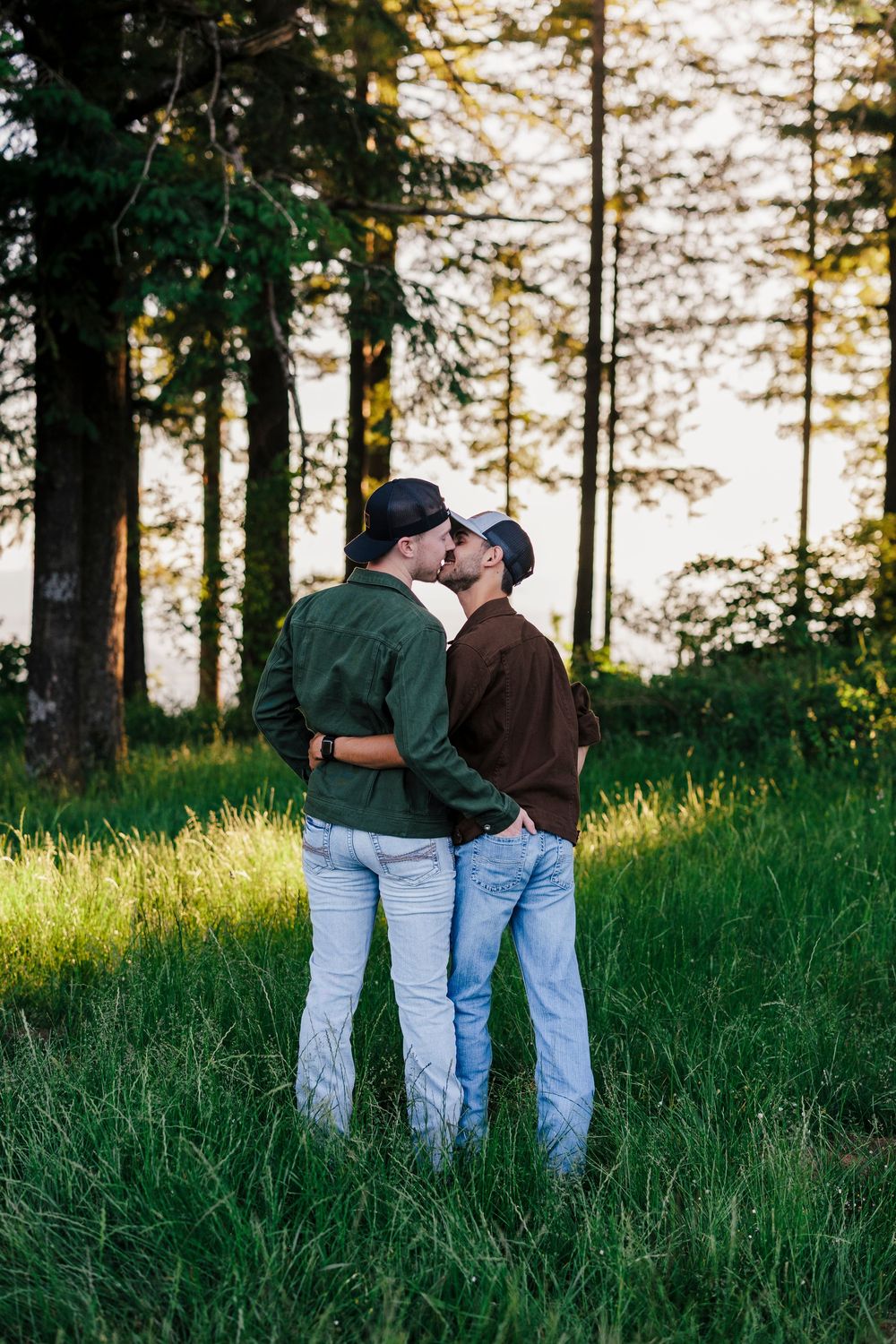 A couple sharing an intimate moment together in a sunlit forest with tall evergreen trees.