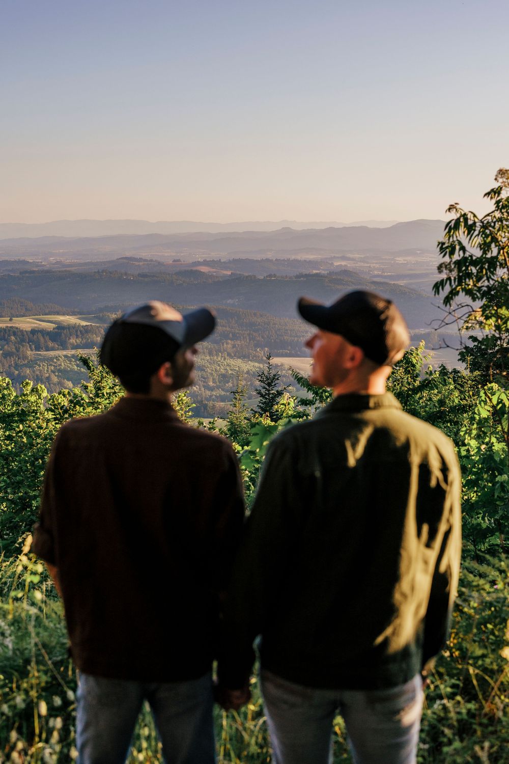 Silhouettes of people admiring a scenic mountain vista from a hilltop lookout point.