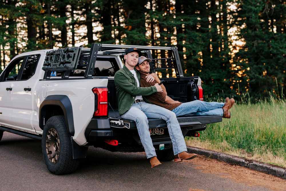 Couple enjoying a sunset while sitting in the back of a white pickup truck on a forest road.