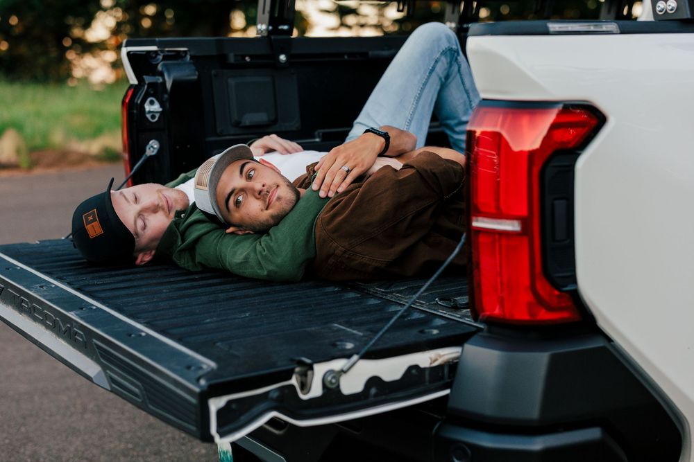 A person relaxes in casual attire while lying in the bed of a pickup truck on a sunny afternoon.