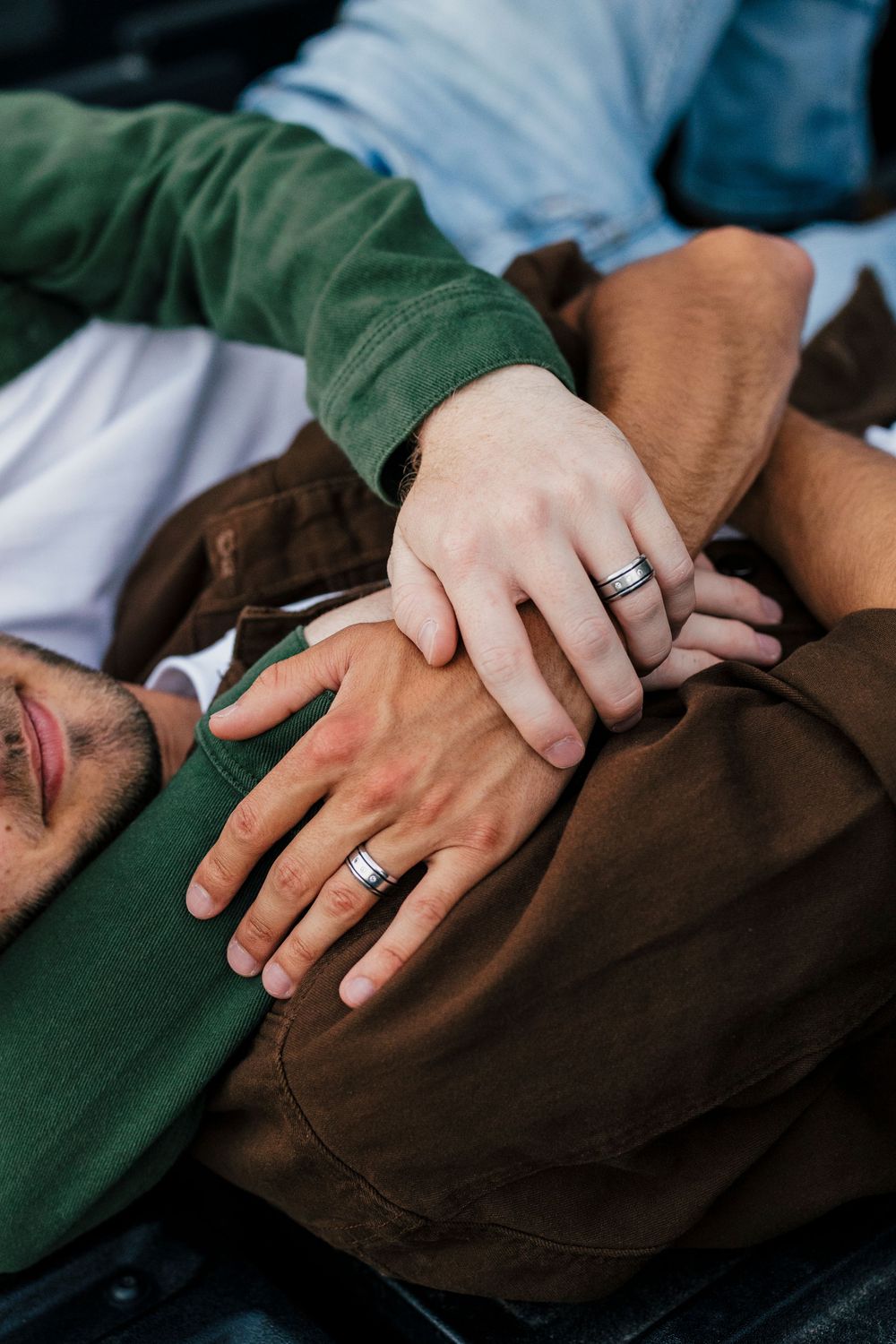 Closeup of hands gently touching and showing a wedding ring against a dark fabric background.