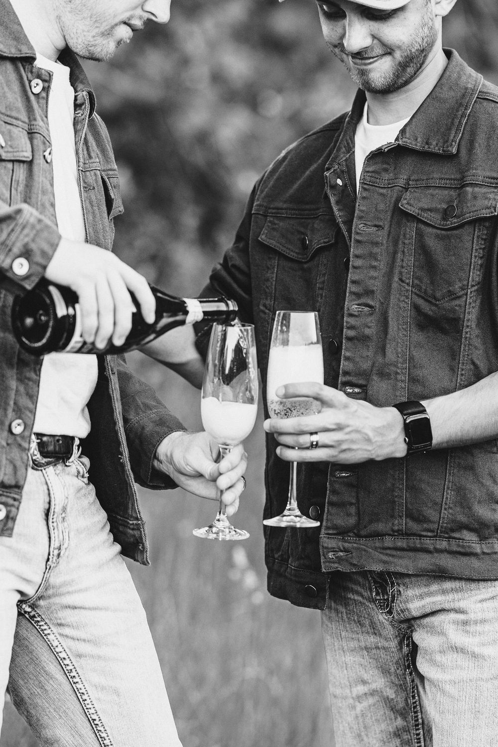 Close-up black and white photo of champagne being poured into flutes held by people wearing denim jackets.