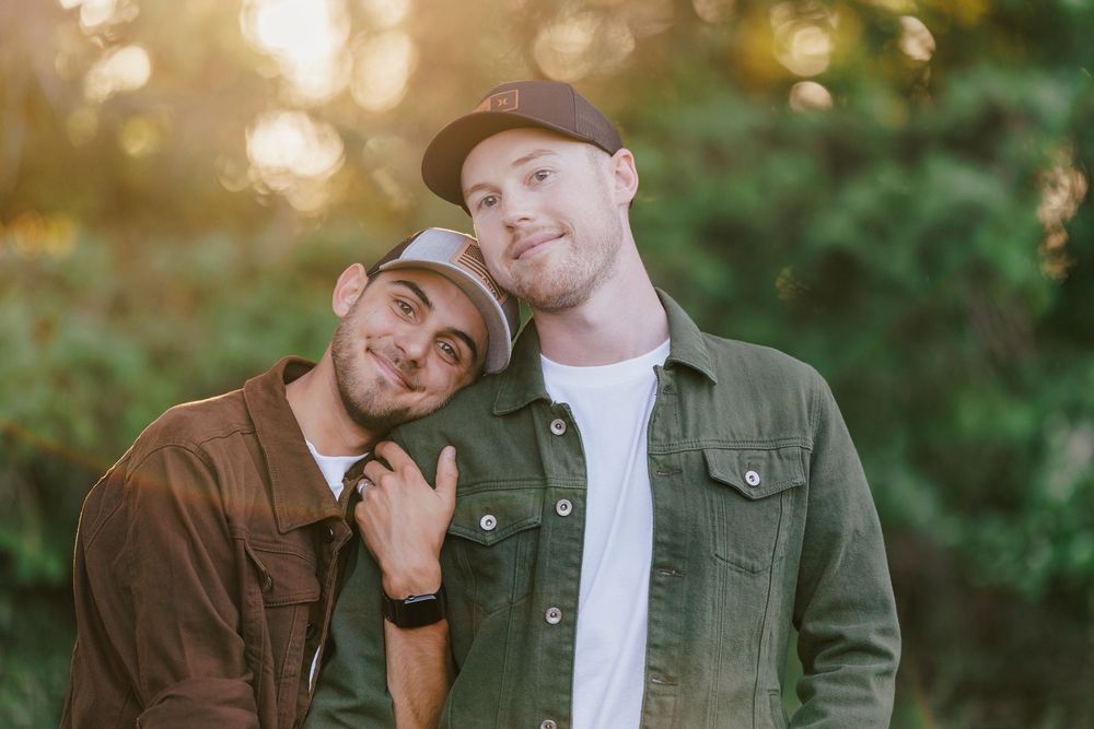 Couple in casual attire posing together outdoors with warm sunlit bokeh in the background.