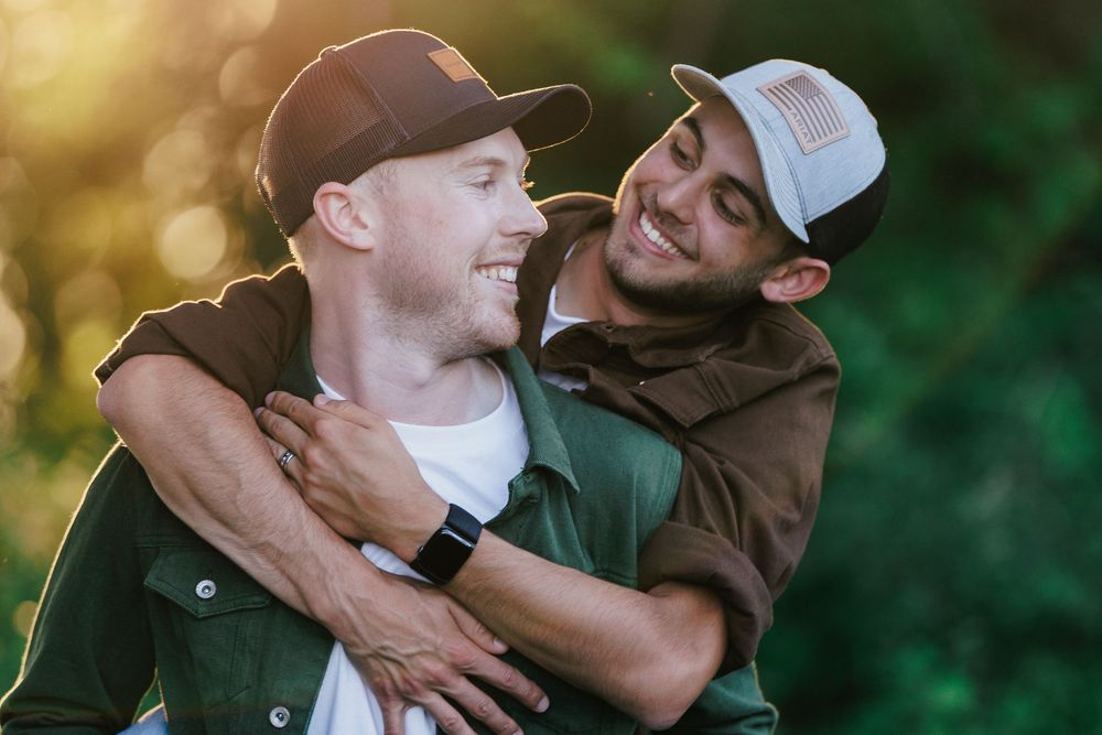 Two friends laugh and embrace outdoors during golden hour with a green natural background.