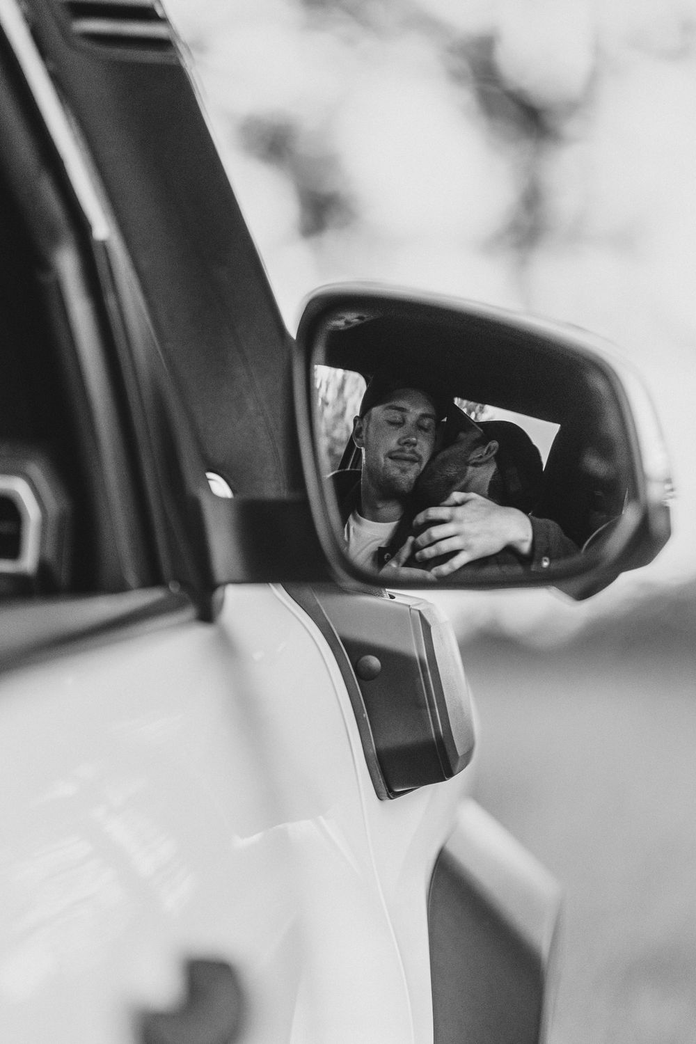 Black and white reflection in car side mirror showing two people in an intimate moment.