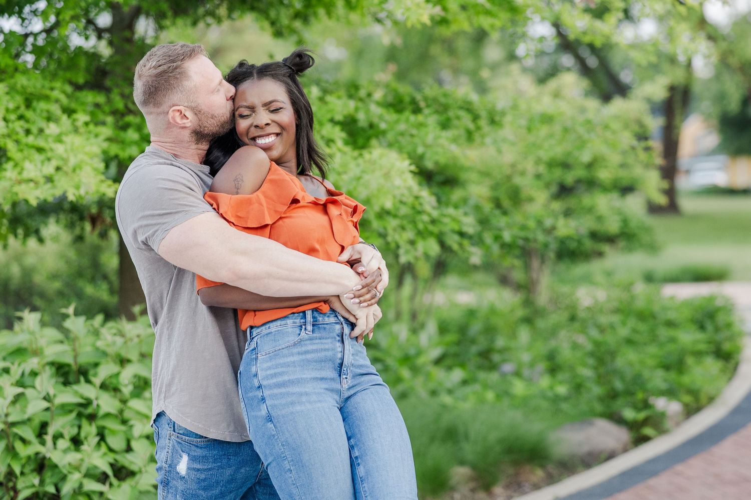 Loving couple embraces while taking romantic engagement photos in a lush green garden setting.