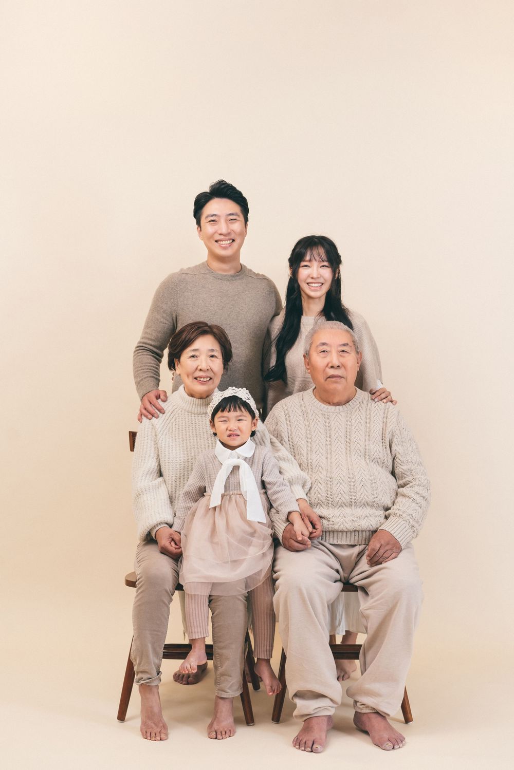 Multi-generational family portrait in coordinated neutral sweaters against beige background.