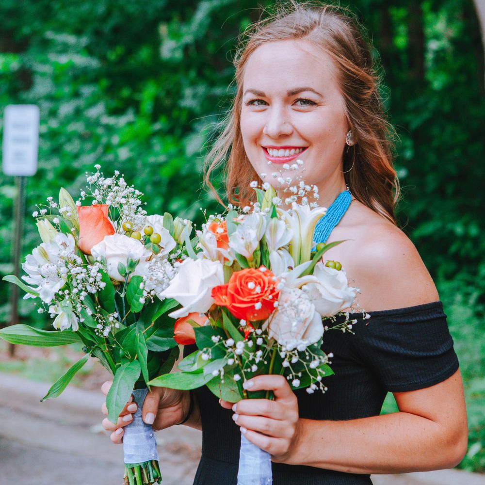 Bride in black off-shoulder dress holding colorful bouquet of roses and lilies.