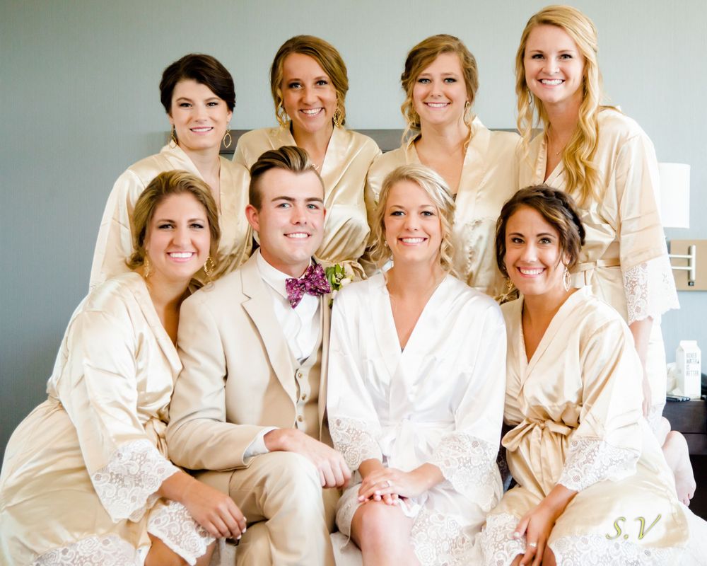 A wedding party group wearing cream colored silk robes poses together in a bright room before the ceremony.