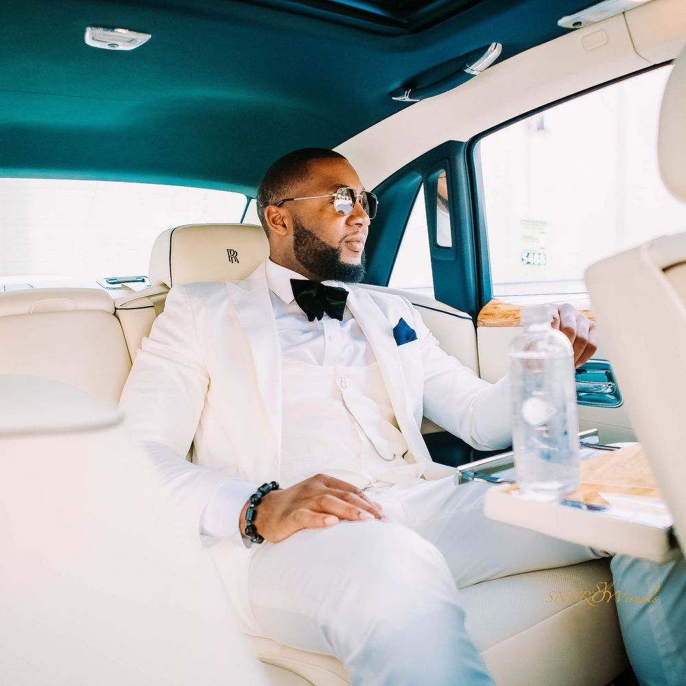 Person in crisp white suit relaxing in luxury vehicle with refreshment.