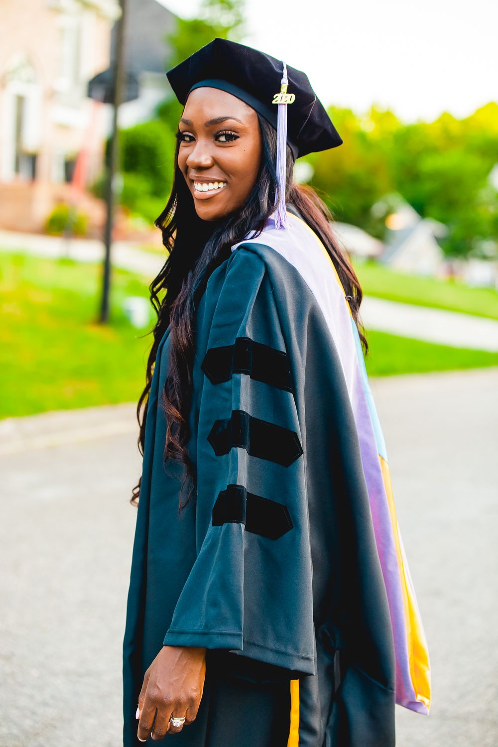 Graduate in ceremonial doctoral gown and cap poses with bright smile outdoors.