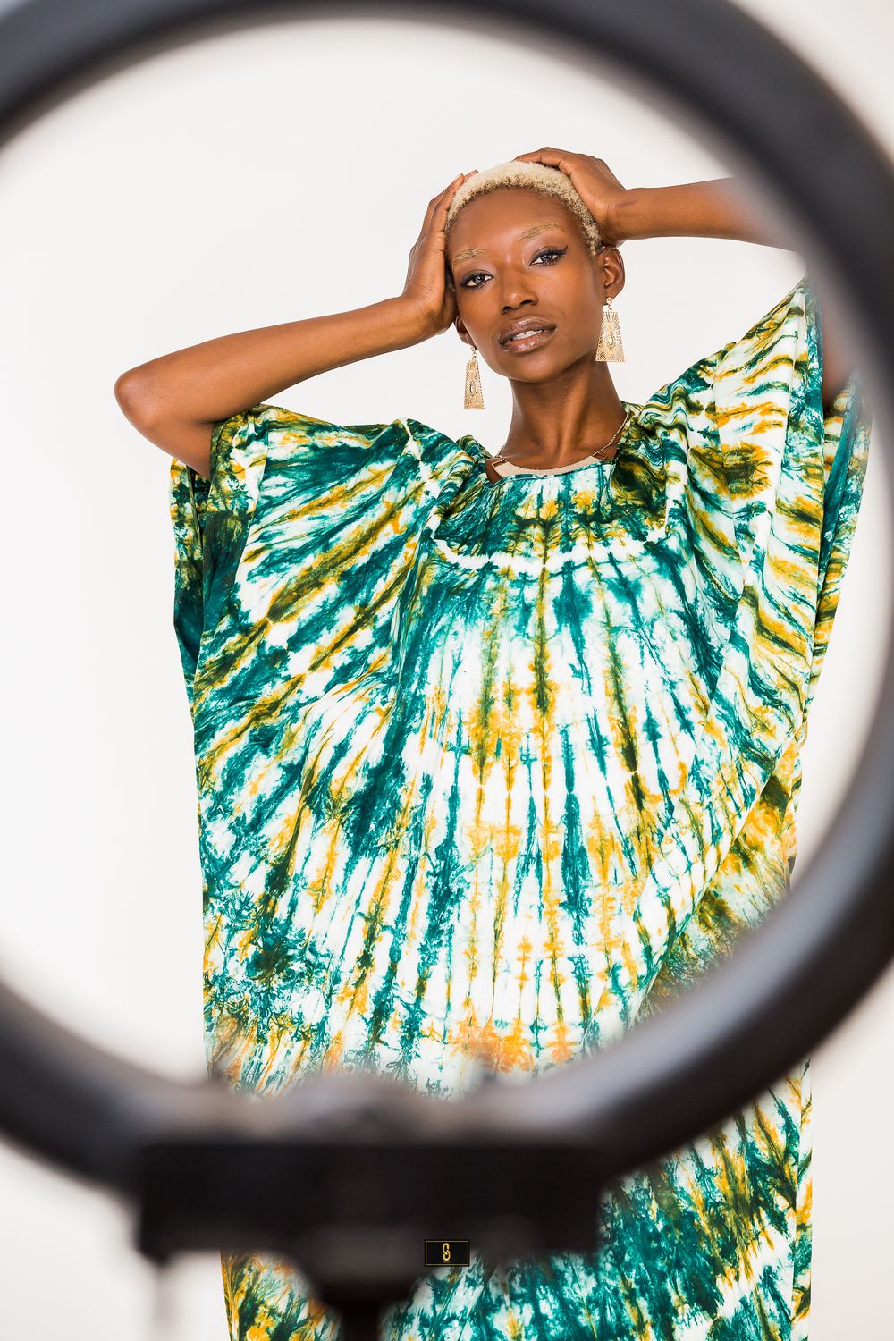 Creative shot through ring light of model in green and yellow tie-dye kaftan dress.