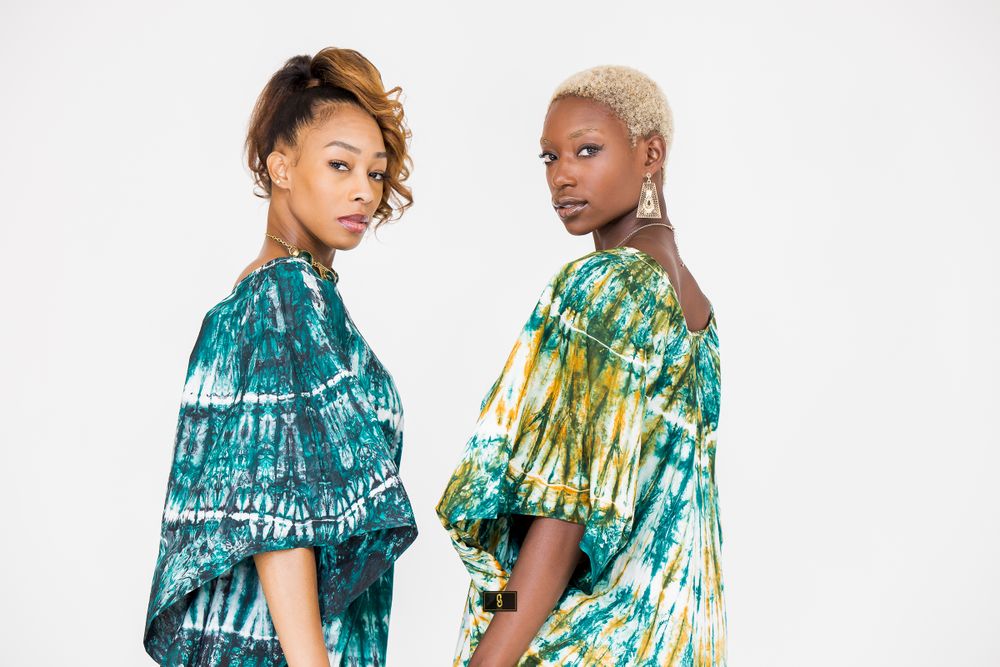 Two models pose side by side wearing coordinating teal and yellow-green tie-dye dresses.