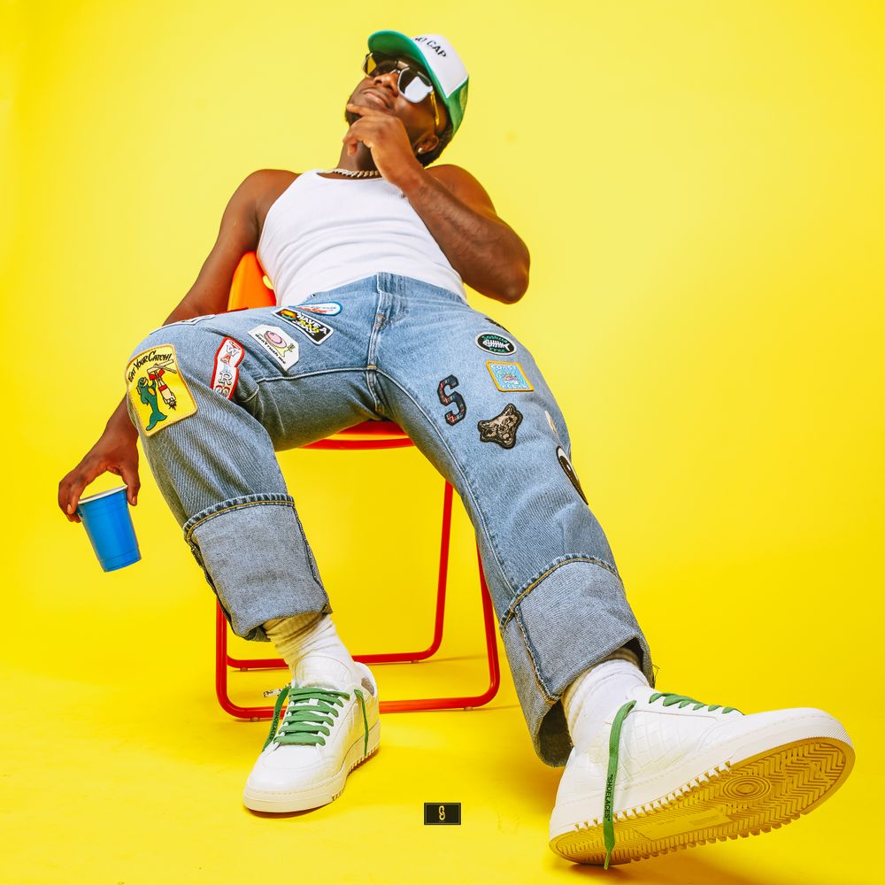 Low angle shot of model relaxing in distressed jeans and white tank on orange chair with blue drink.