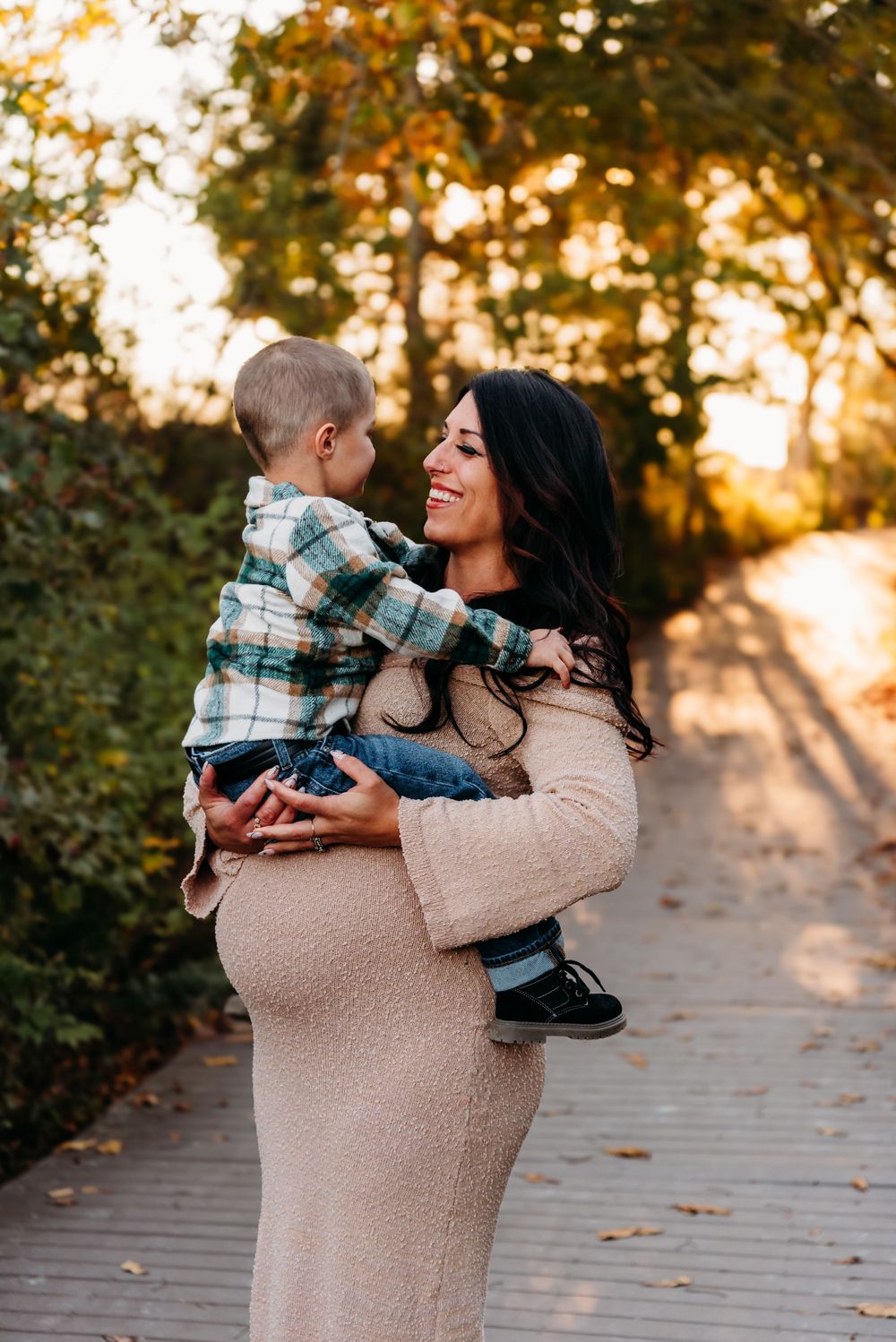 A tender moment at sunset on a wooden boardwalk as a woman in a beige dress holds a small child wearing plaid.