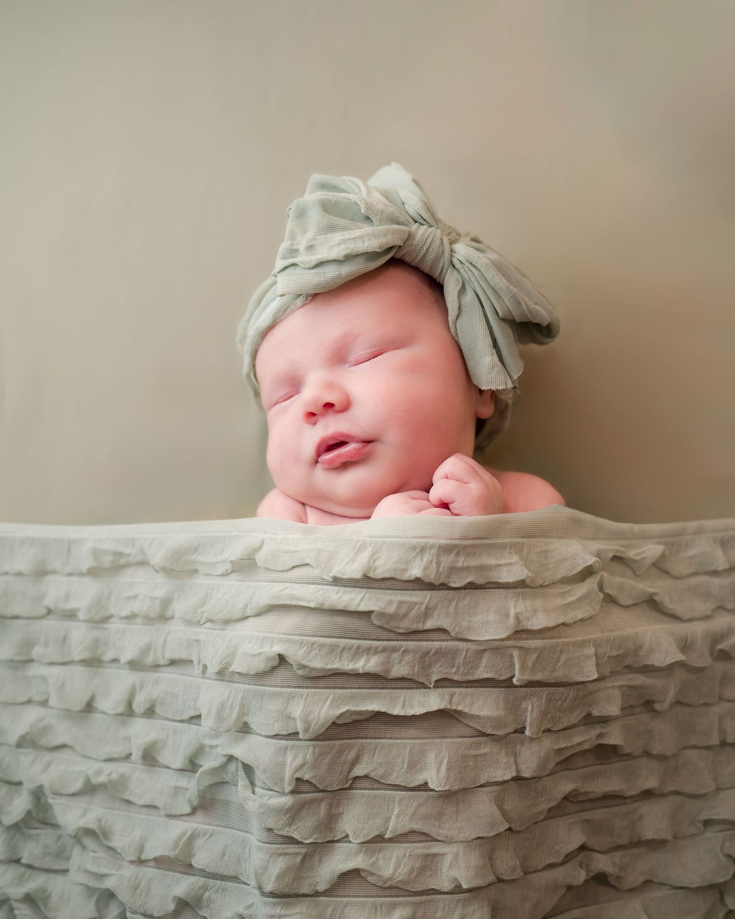 A sleeping newborn lying on textured grey fabric wearing a light colored bow headband.