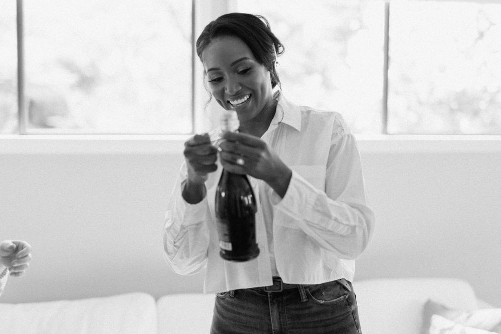 Black and white photo of someone in a white button down shirt smiling while looking down at a bottle.