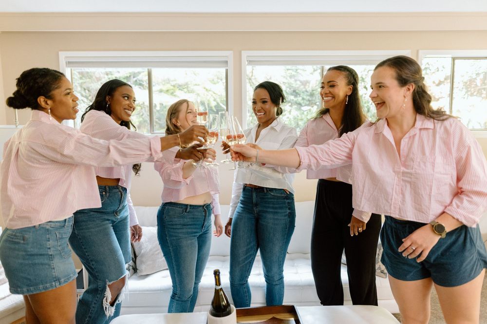 A group of friends in coordinated pink shirts and denim share a celebratory toast together in a bright room.