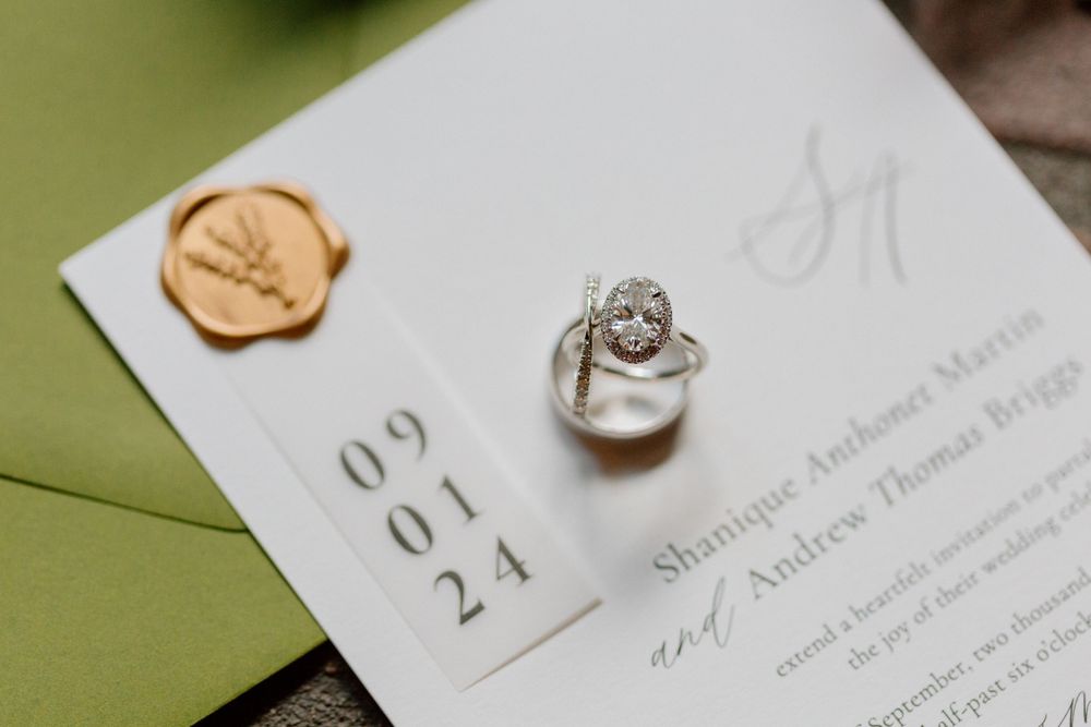 Wedding invitation with date 09.01.24 alongside an engagement ring and gold wax seal on green envelope.