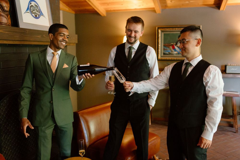 Three groomsmen in formal attire share a lighthearted moment while getting ready before a wedding ceremony.