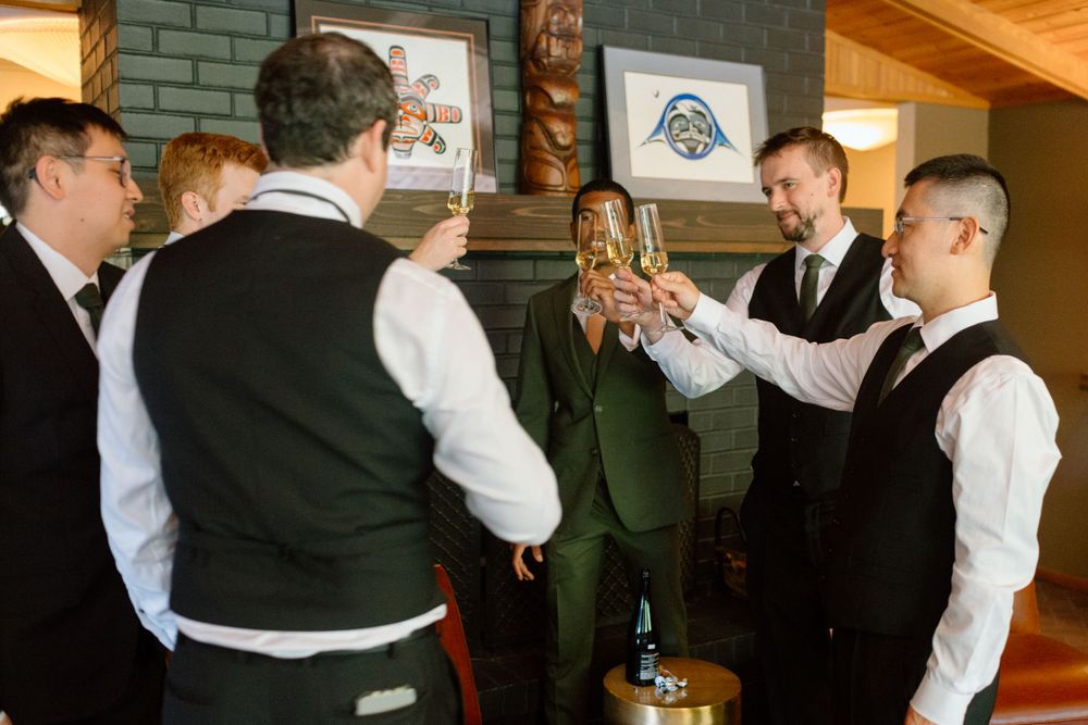 A group of well-dressed people in vests and formal attire raise their glasses in a celebratory toast indoors.