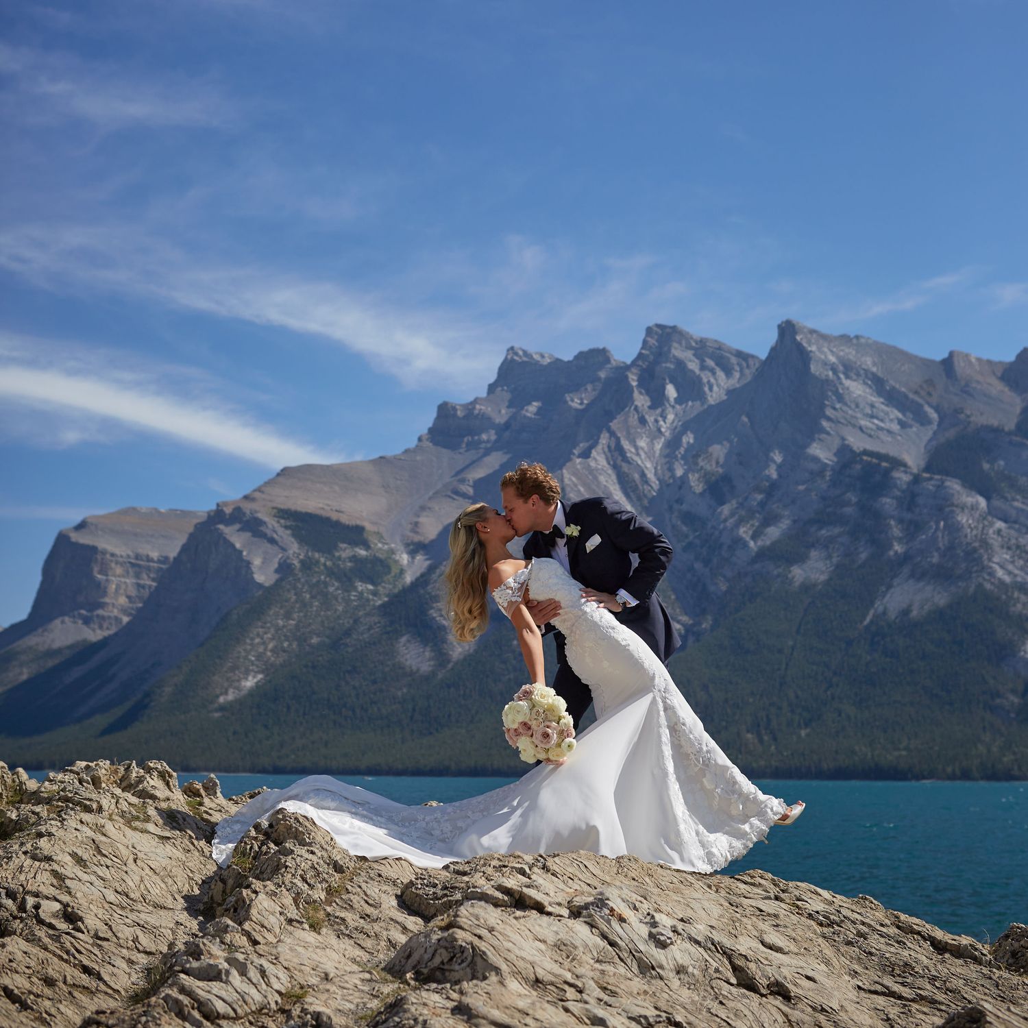 A couple share a romantic moment on a mountain overlooking Lake Minnewanka and Two Jack Lake in the Canadian Rockies in Banff National Park.