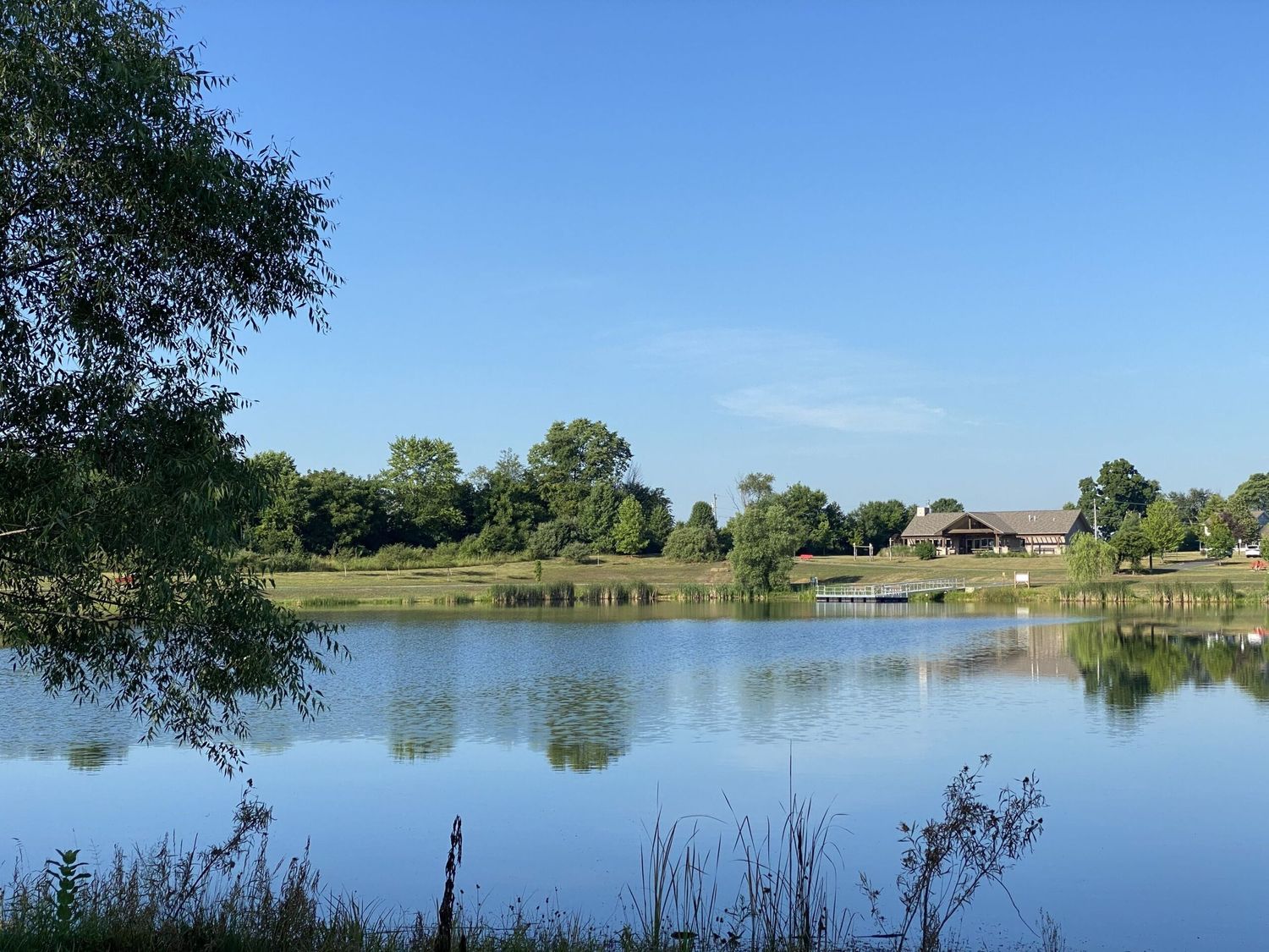 A peaceful lake reflects the blue sky while rustic buildings and trees line the tranquil shoreline on a sunny day.