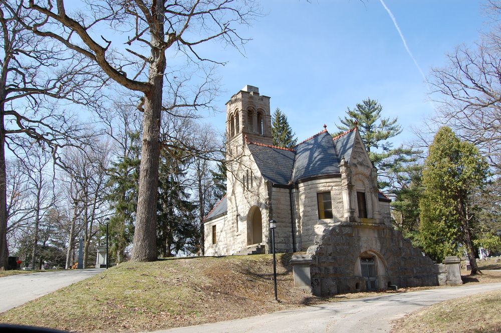 A small Gothic-style stone chapel with a bell tower stands on a wooded hillside along a winding path.