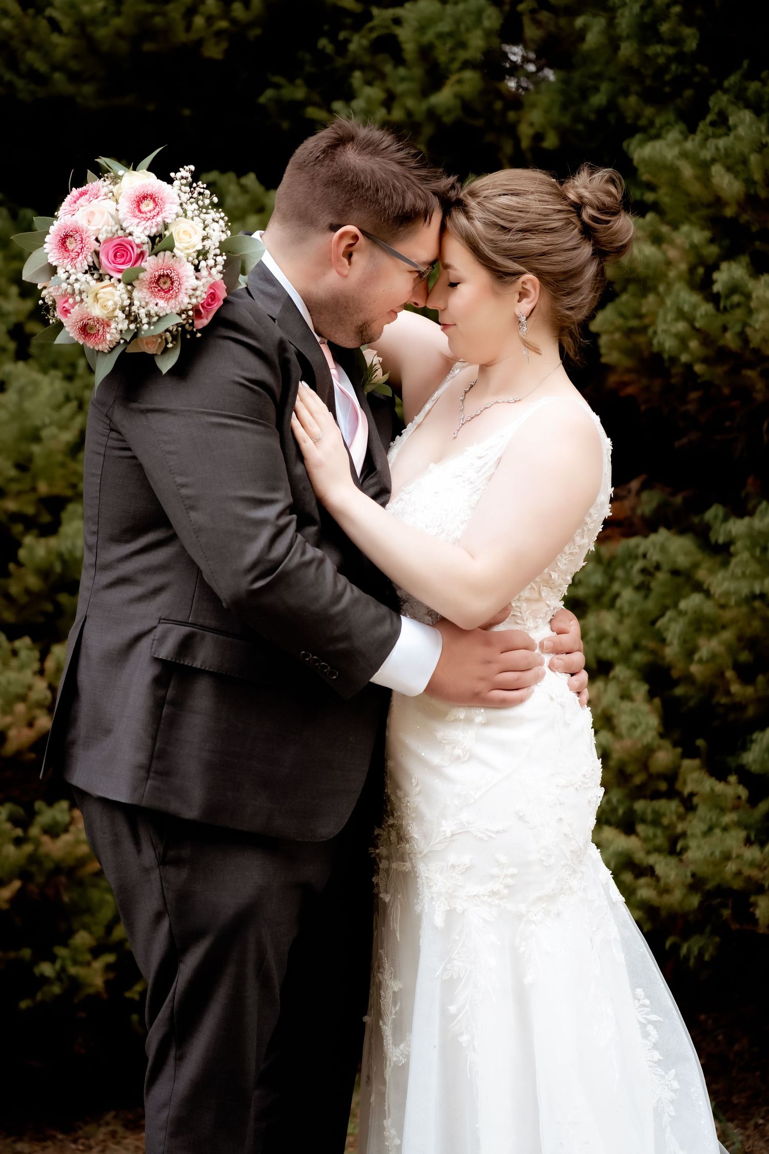 A romantic wedding moment with a bridal couple embracing outdoors, featuring a pink and white rose bouquet.