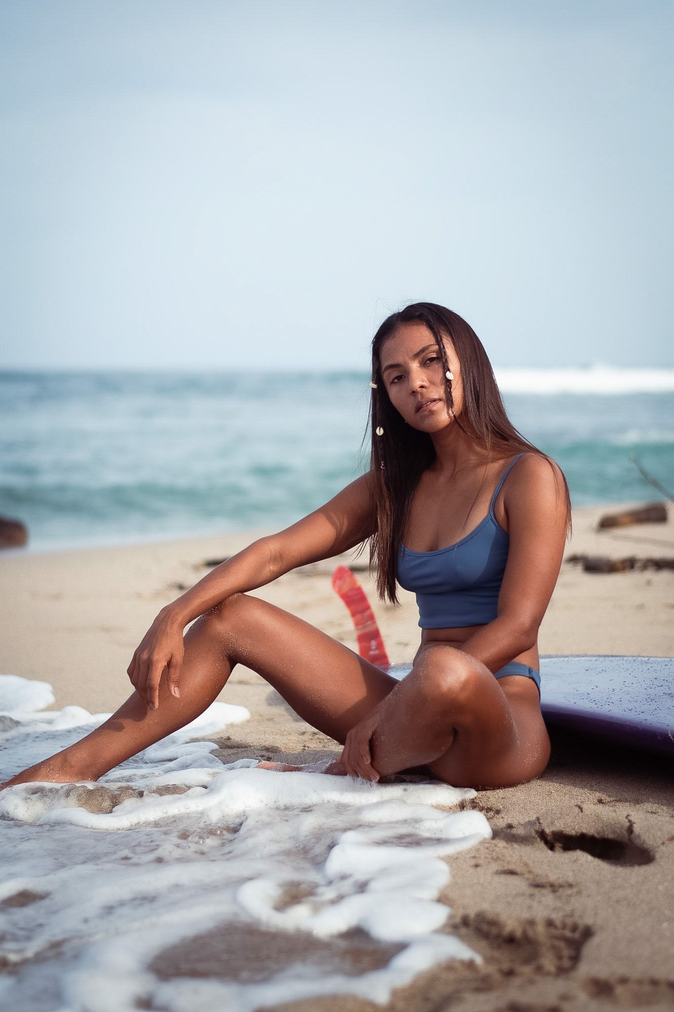 Woman in blue swimsuit sitting on sandy beach with ocean waves and coastline in background.