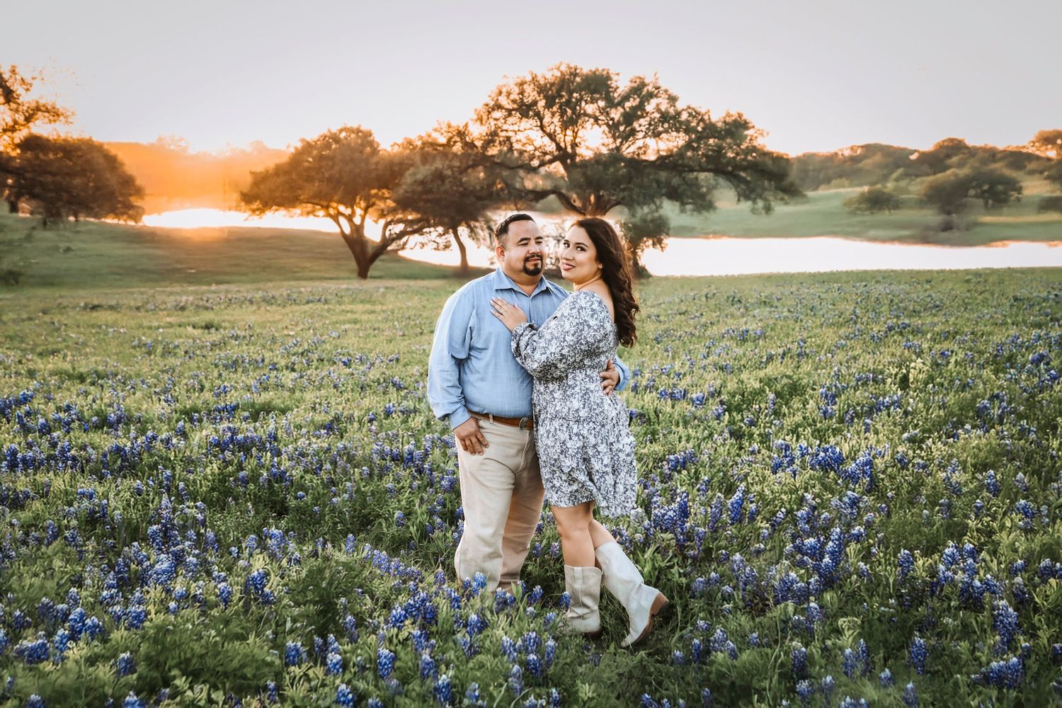 Fiancé lifts bride-to-be for a kiss in a sea of Texas bluebonnets with the lake sparkling in the background