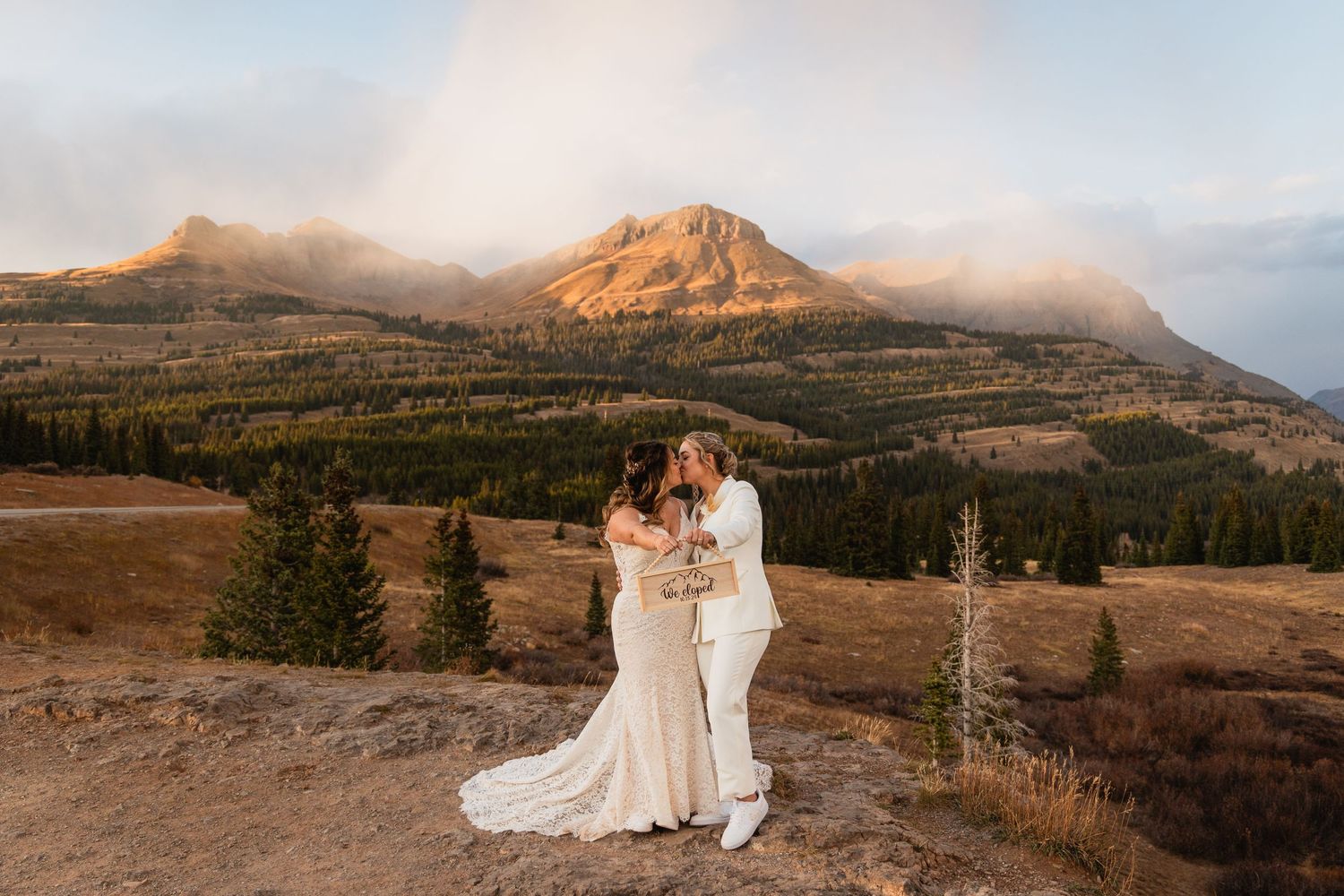 Two people embrace during a sunset wedding photoshoot with a majestic mountain peak and fog in the background.