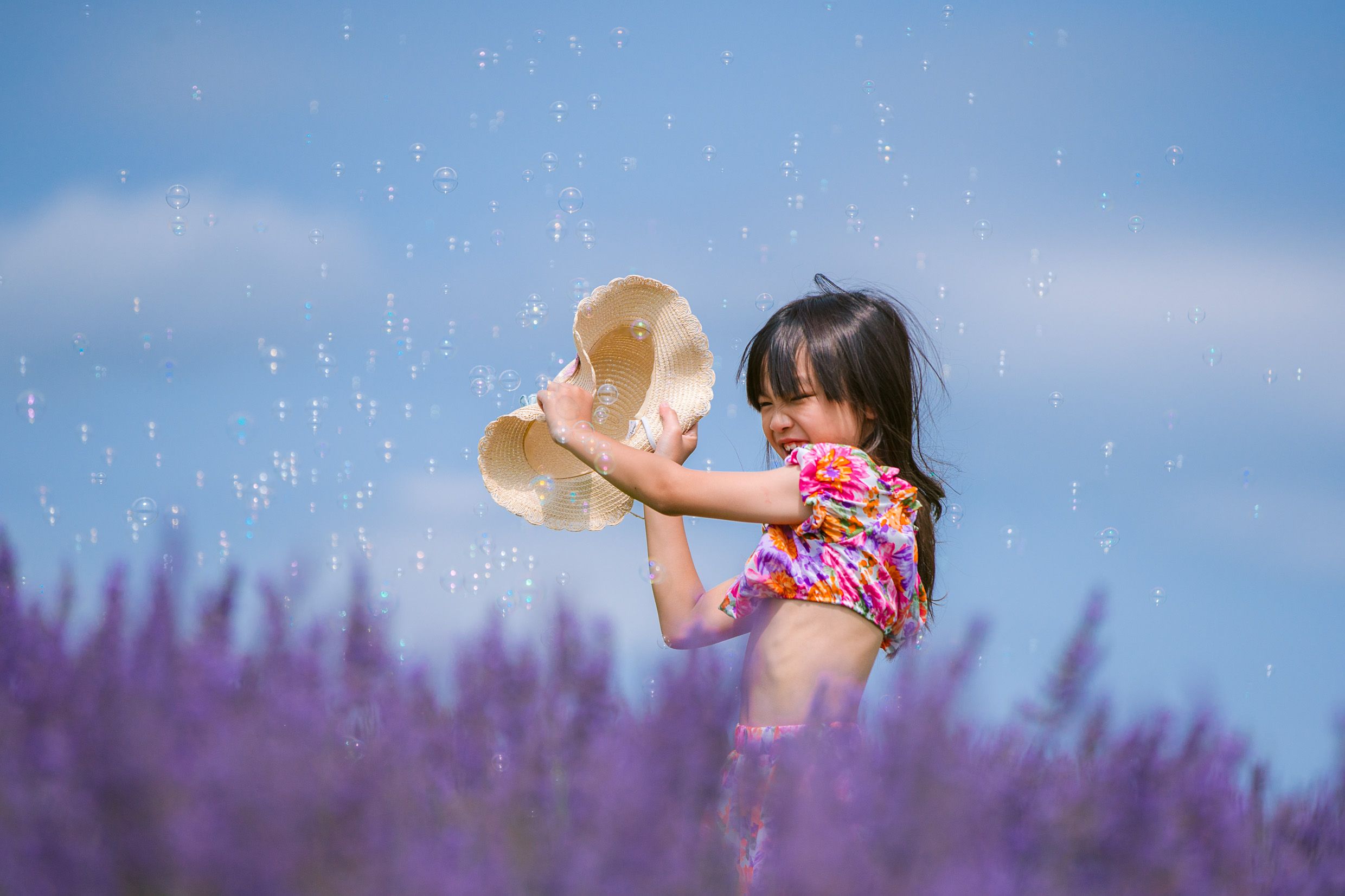 Playing with bubbles in a vibrant purple lavender field against a bright blue summer sky.