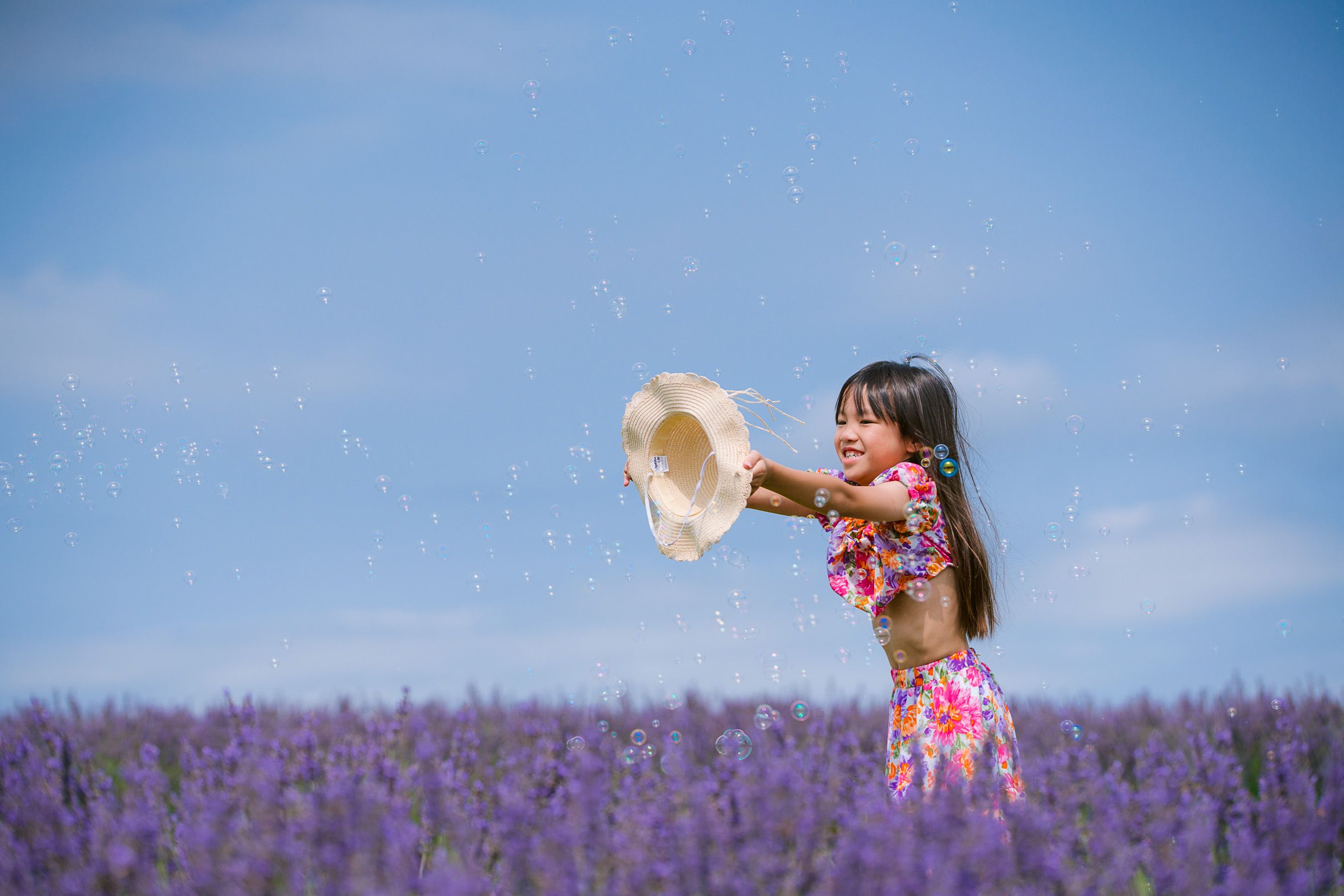 A dreamy summer scene in a purple lavender field with a sun hat being tossed into the bright blue sky.