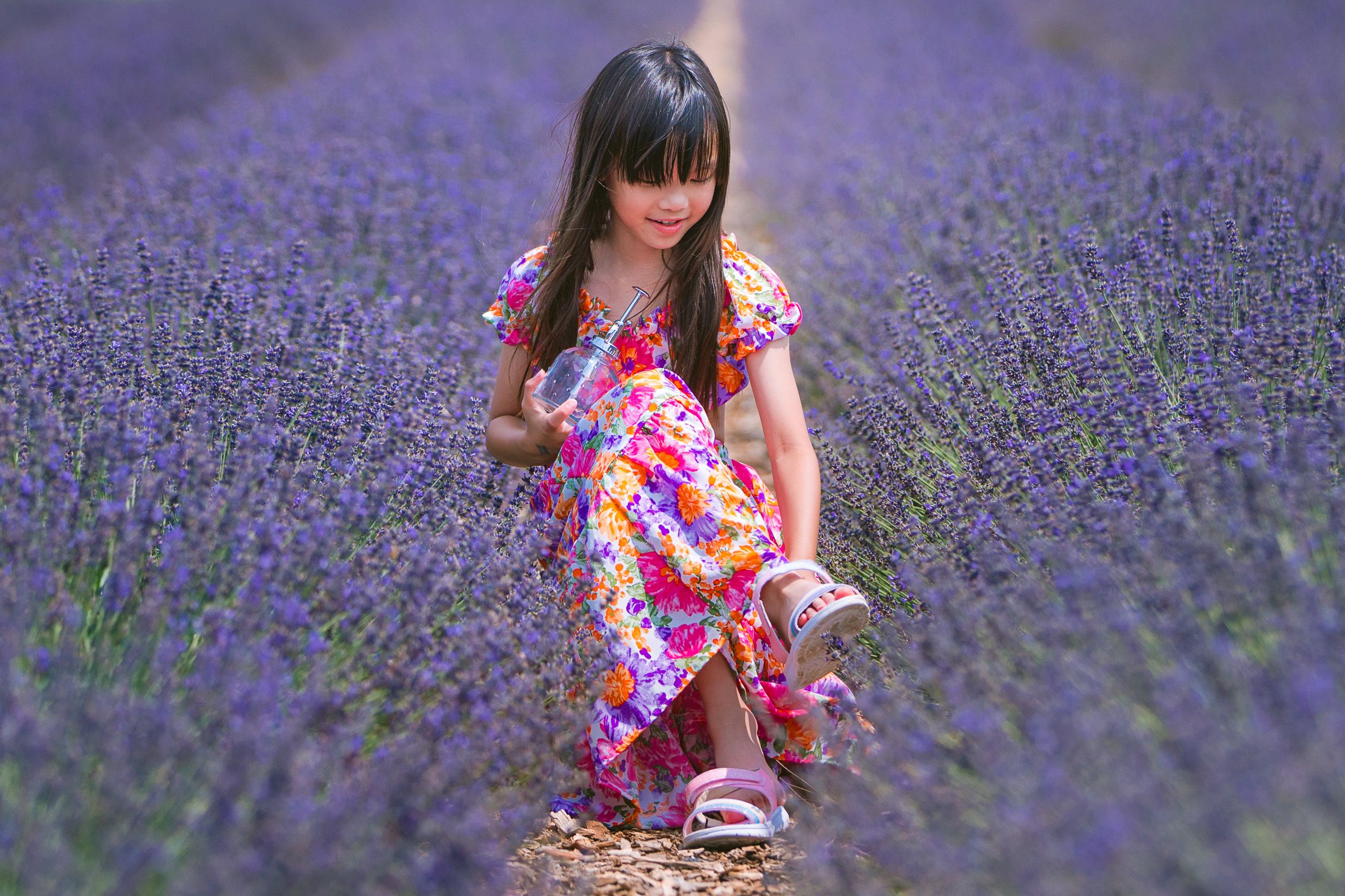 Young girl in floral dress stands among blooming purple lavender fields on a sunny day.