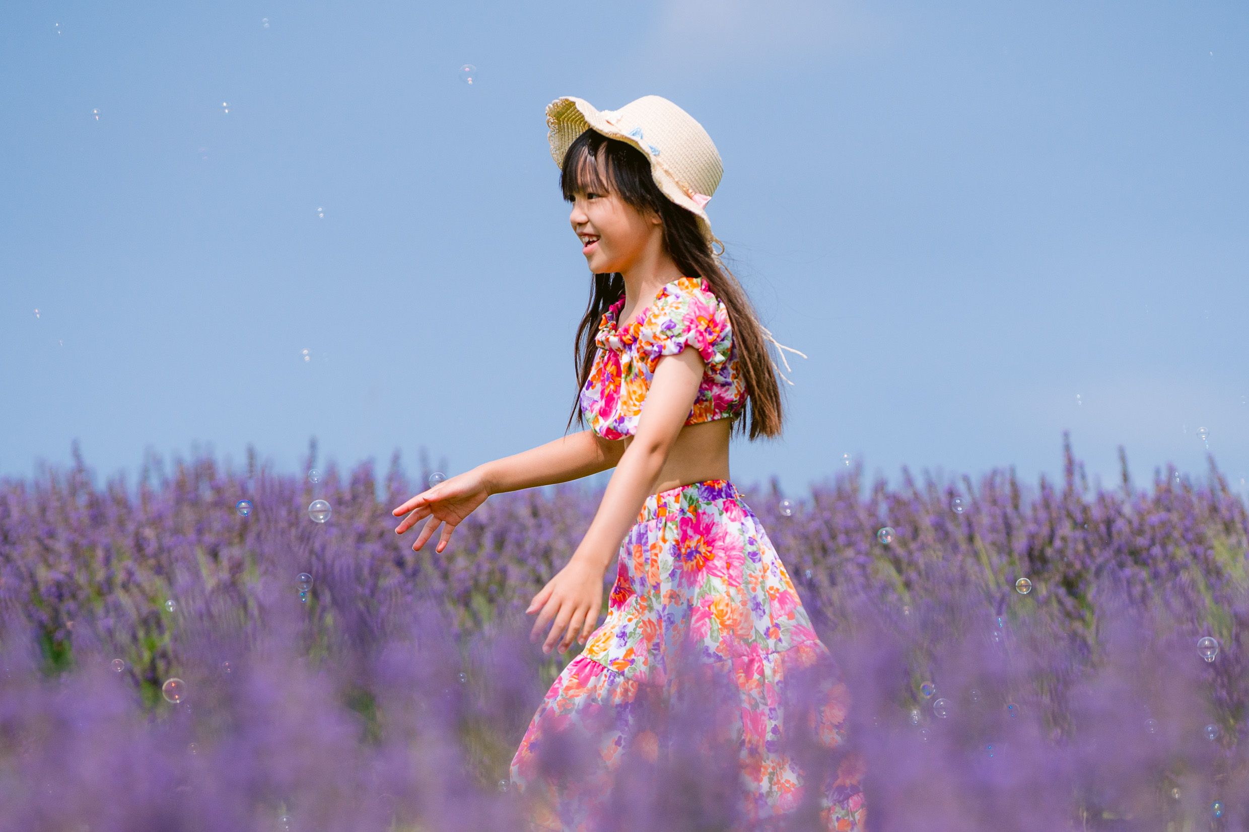 Someone in a floral dress and sun hat spins joyfully in a vibrant purple lavender field on a sunny day.