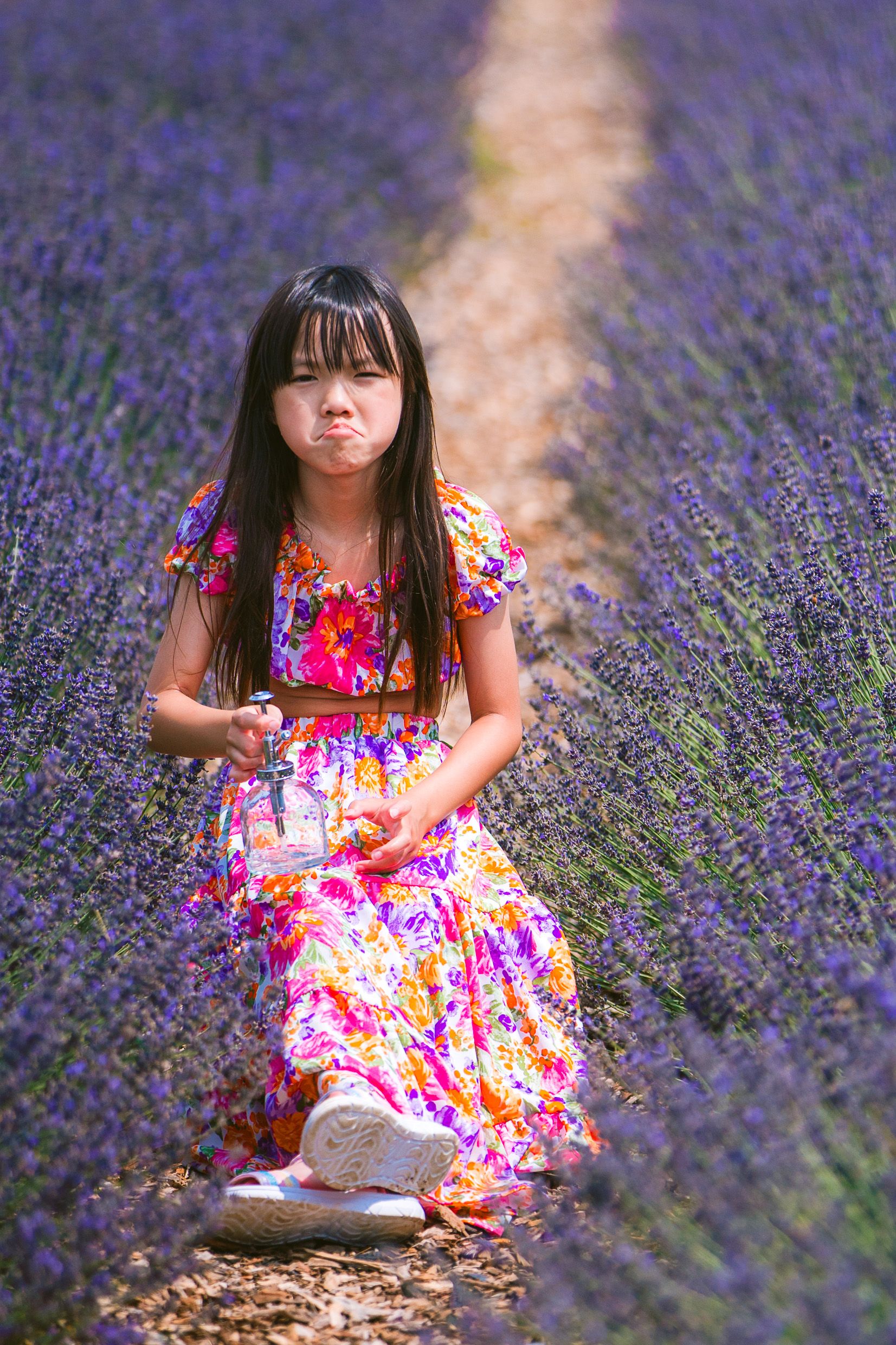 Colorful floral dress stands out among rows of vibrant purple lavender flowers in a scenic garden path.