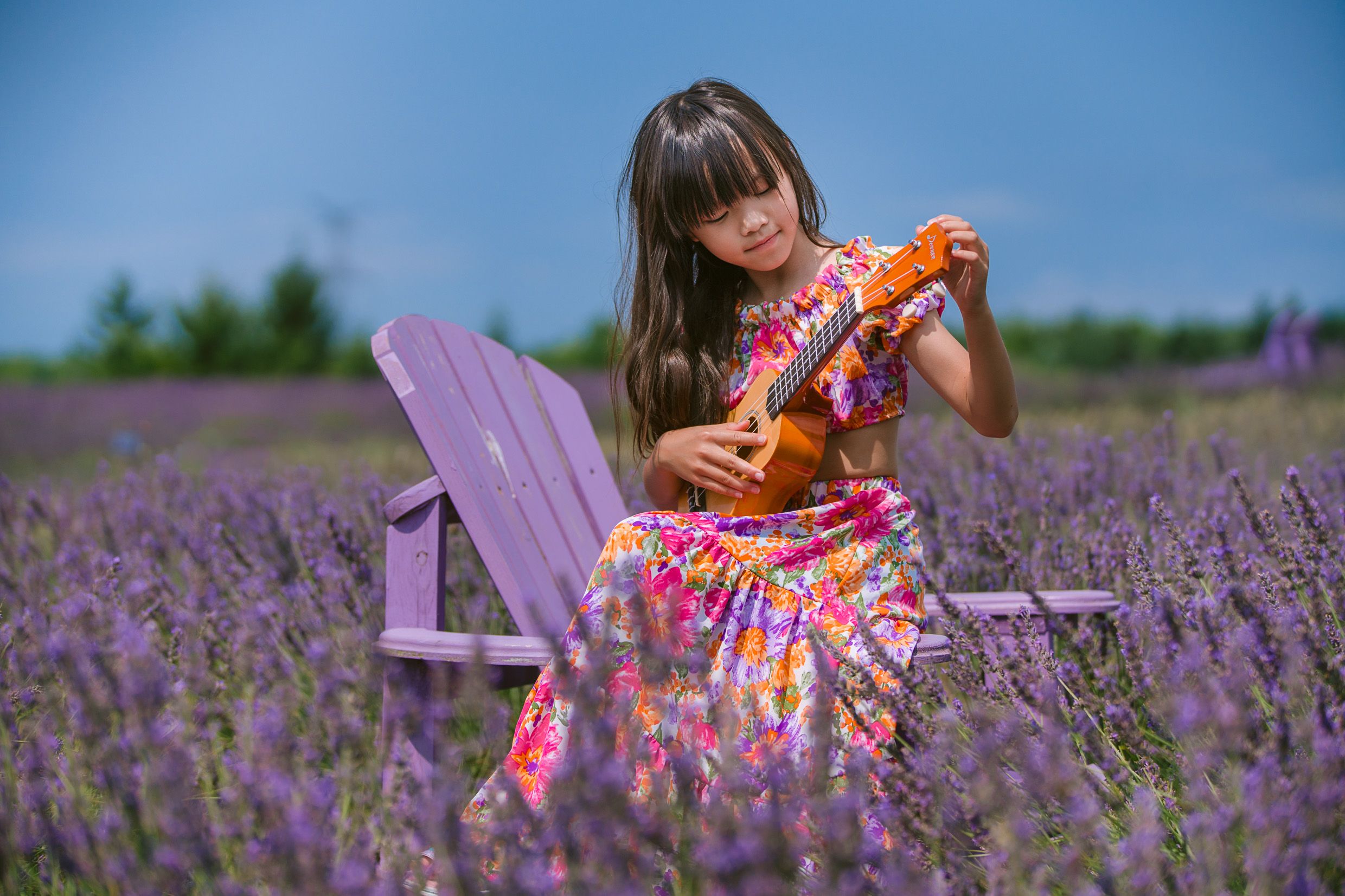 A colorful floral dress stands out against purple lavender fields with a lilac-colored Adirondack chair as backdrop.