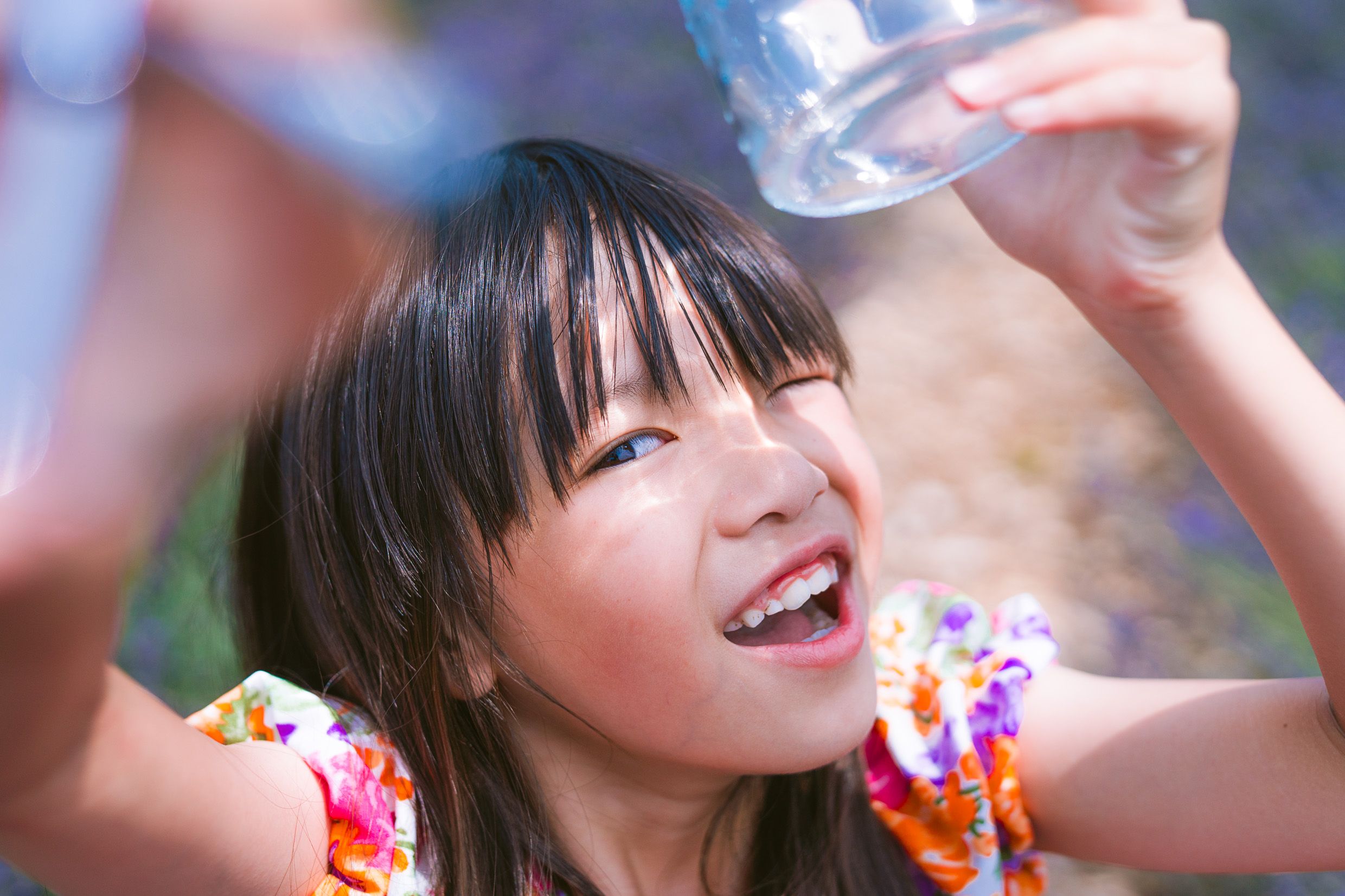 A joyful young child with dark hair raises their hands while wearing a colorful floral print outfit on a sunny day.