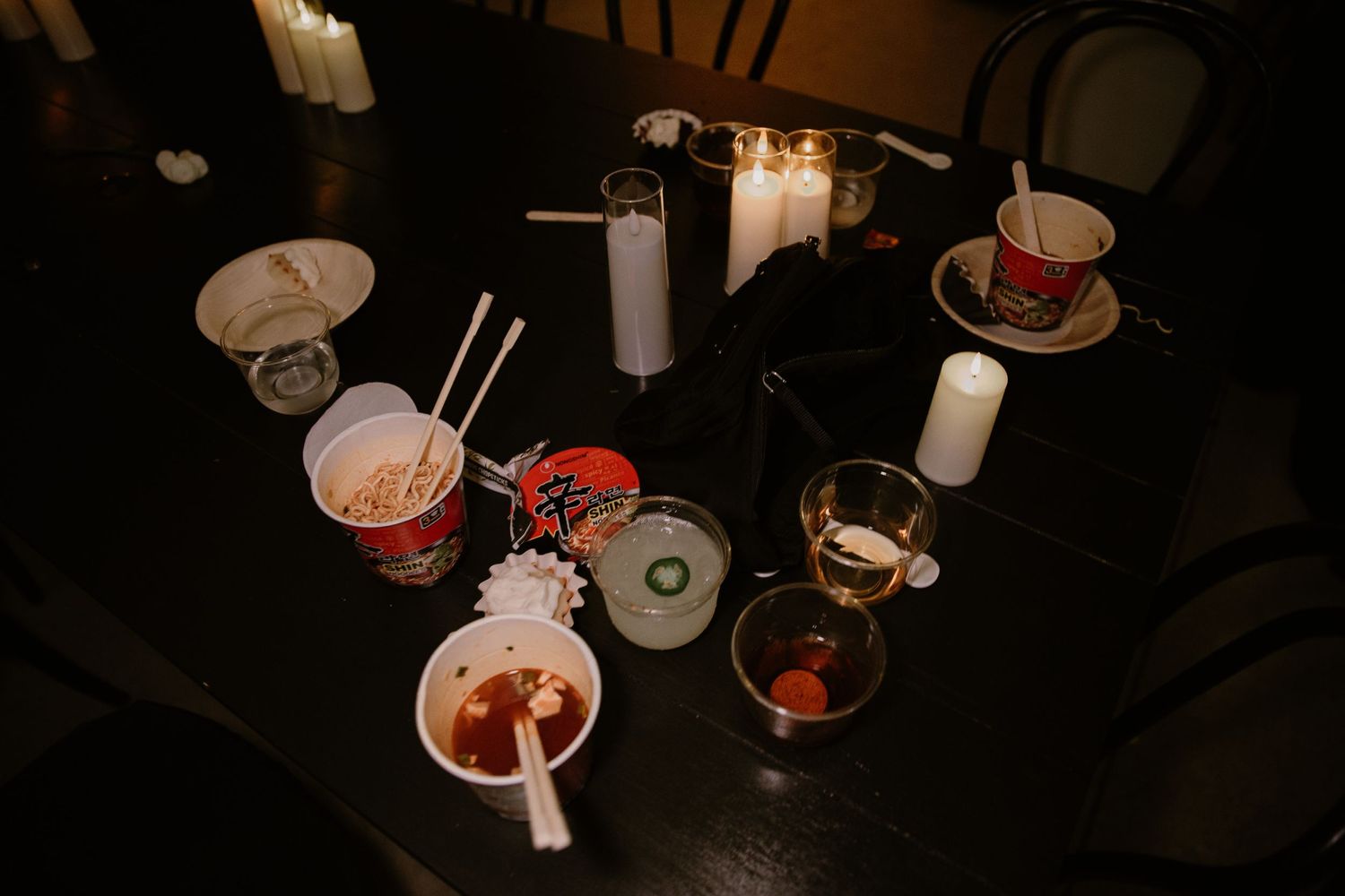 A dark table setting with various cocktail glasses and drinks featuring red garnishes and straws in a dimly lit atmosphere.