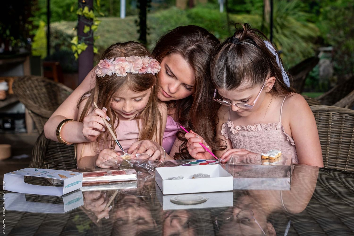 Young children work on arts and crafts together at outdoor table while being supervised.