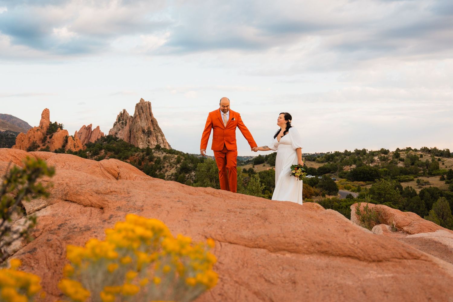 A couple in wedding attire stands on red rocks at Garden of the Gods in Colorado with spires in the background.