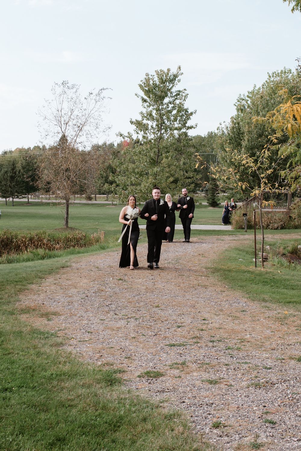 Formal gathering on a gravel path surrounded by autumn trees and greenery in a serene park setting.