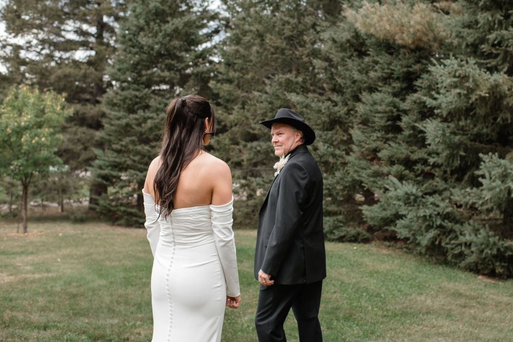 Couple in wedding attire having a private moment outdoors surrounded by evergreen trees.